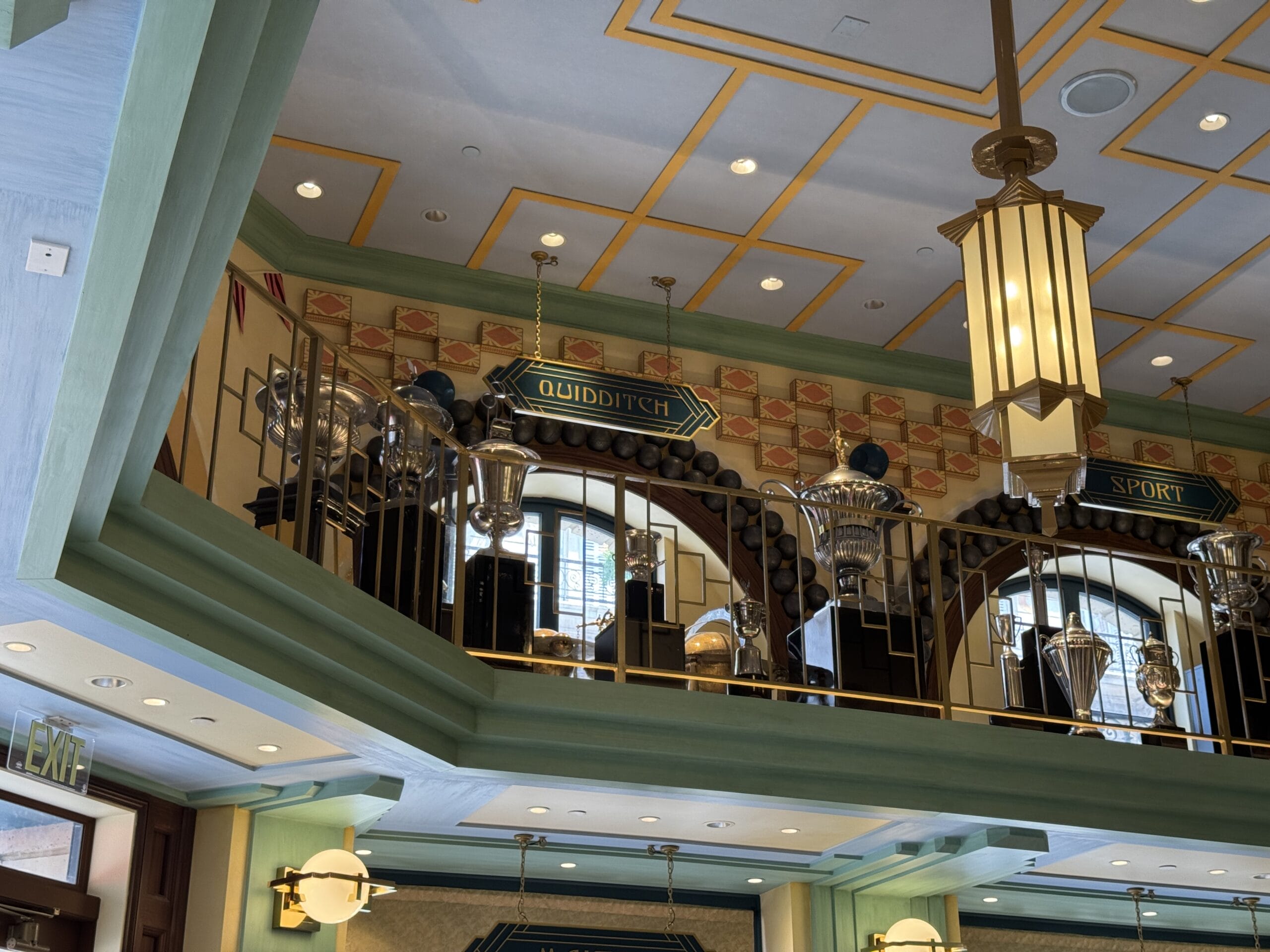Second-floor railing at Les Galeries Mirifiques with "Quidditch," trophies, and vintage decor in a themed interior.