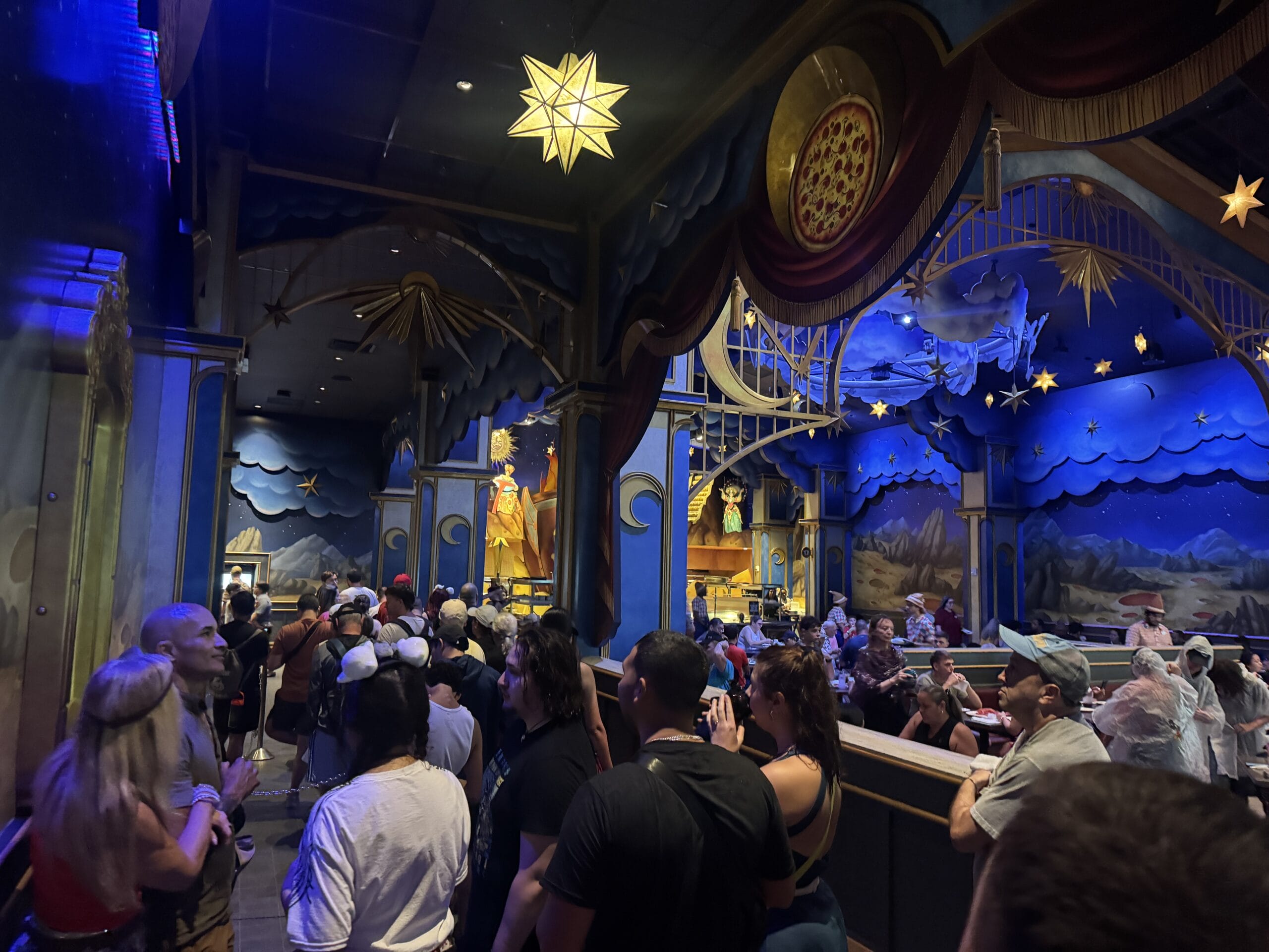 People wait in line inside Epic Universe's colorful, star-themed ride with blue and gold decorations.