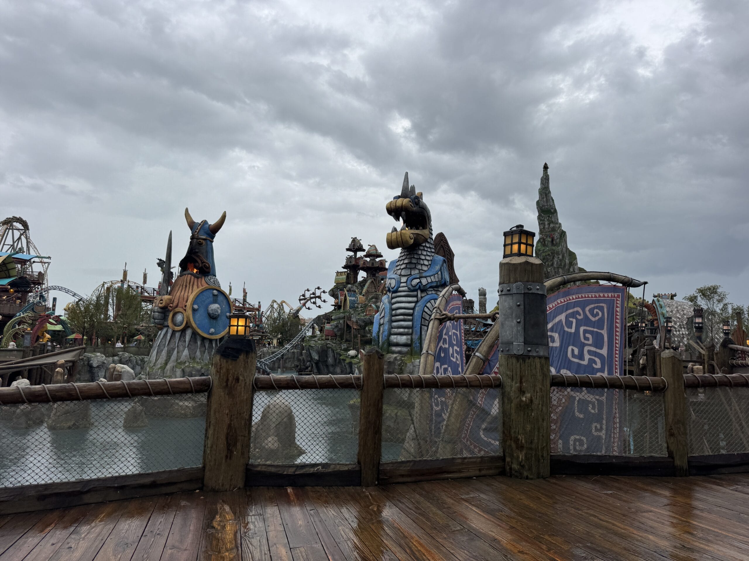Rainy day at Epic Universe: Viking-themed water ride with dragon and warrior ship statues behind a wooden fence.