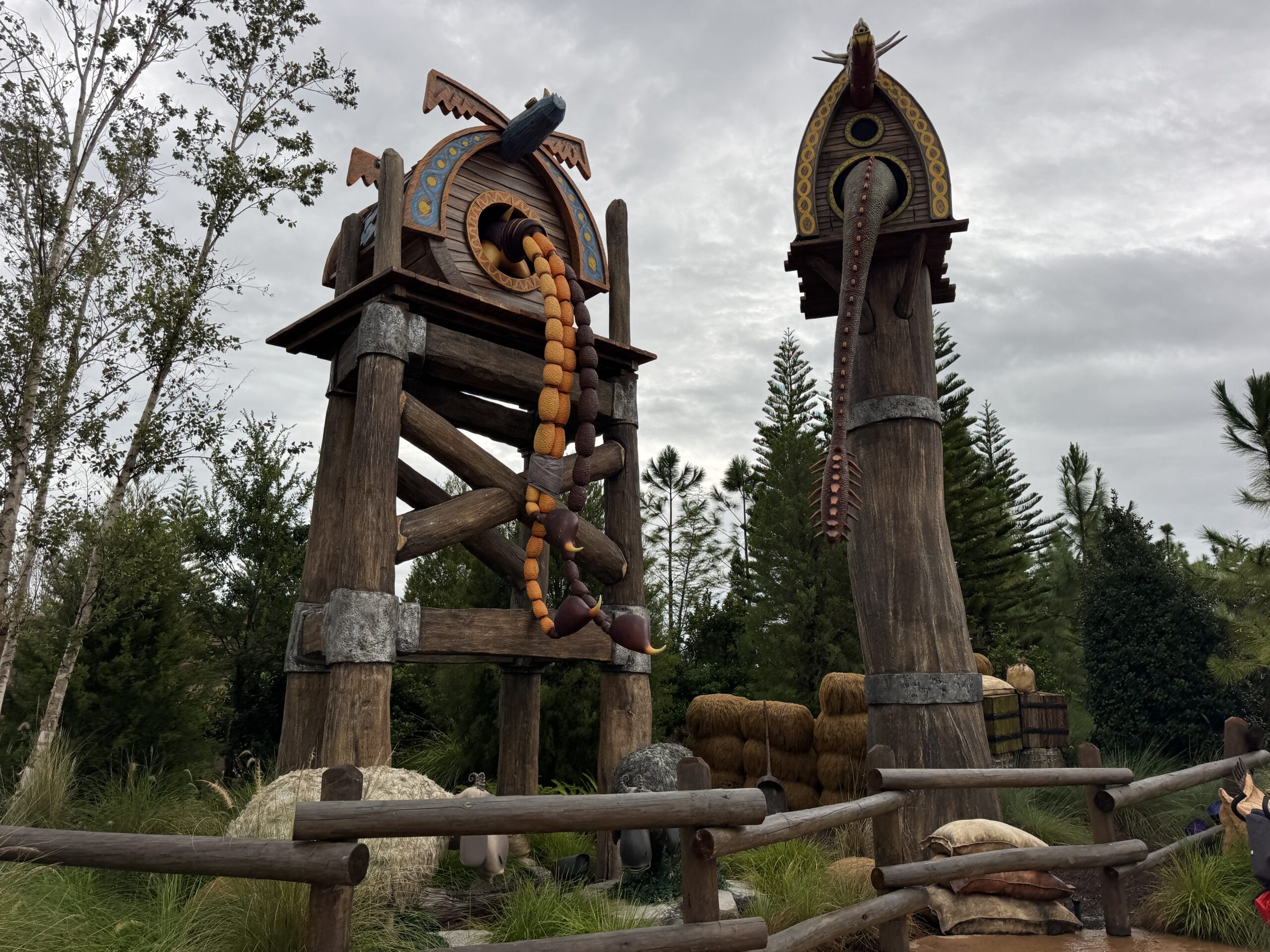 Two large Viking-inspired towers with dragon heads rise among the trees at Epic Universe, under a cloudy sky.