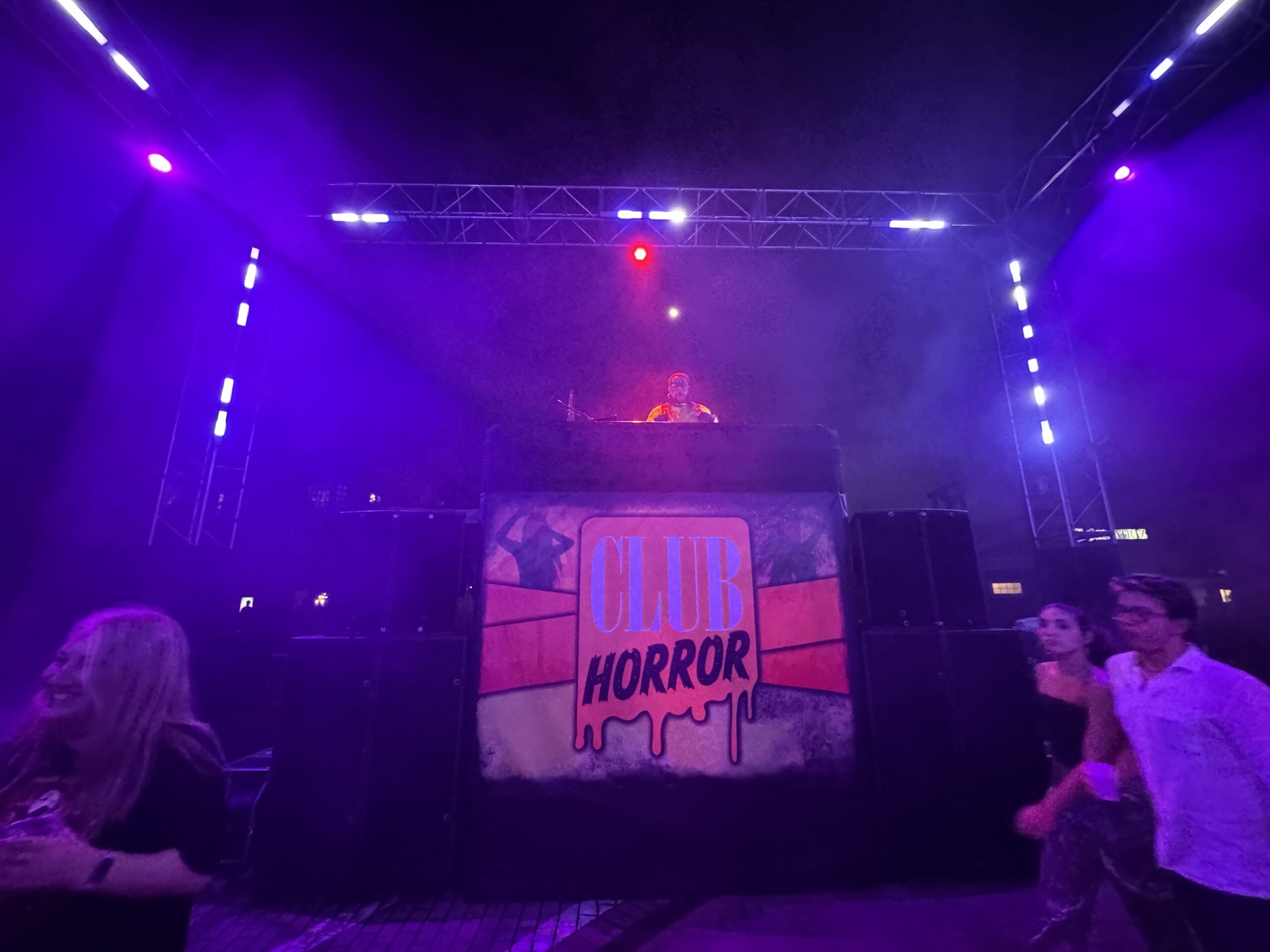 A DJ rocks the stage at Halloween Horror Night's "Club Horror" as people dance under purple lights.