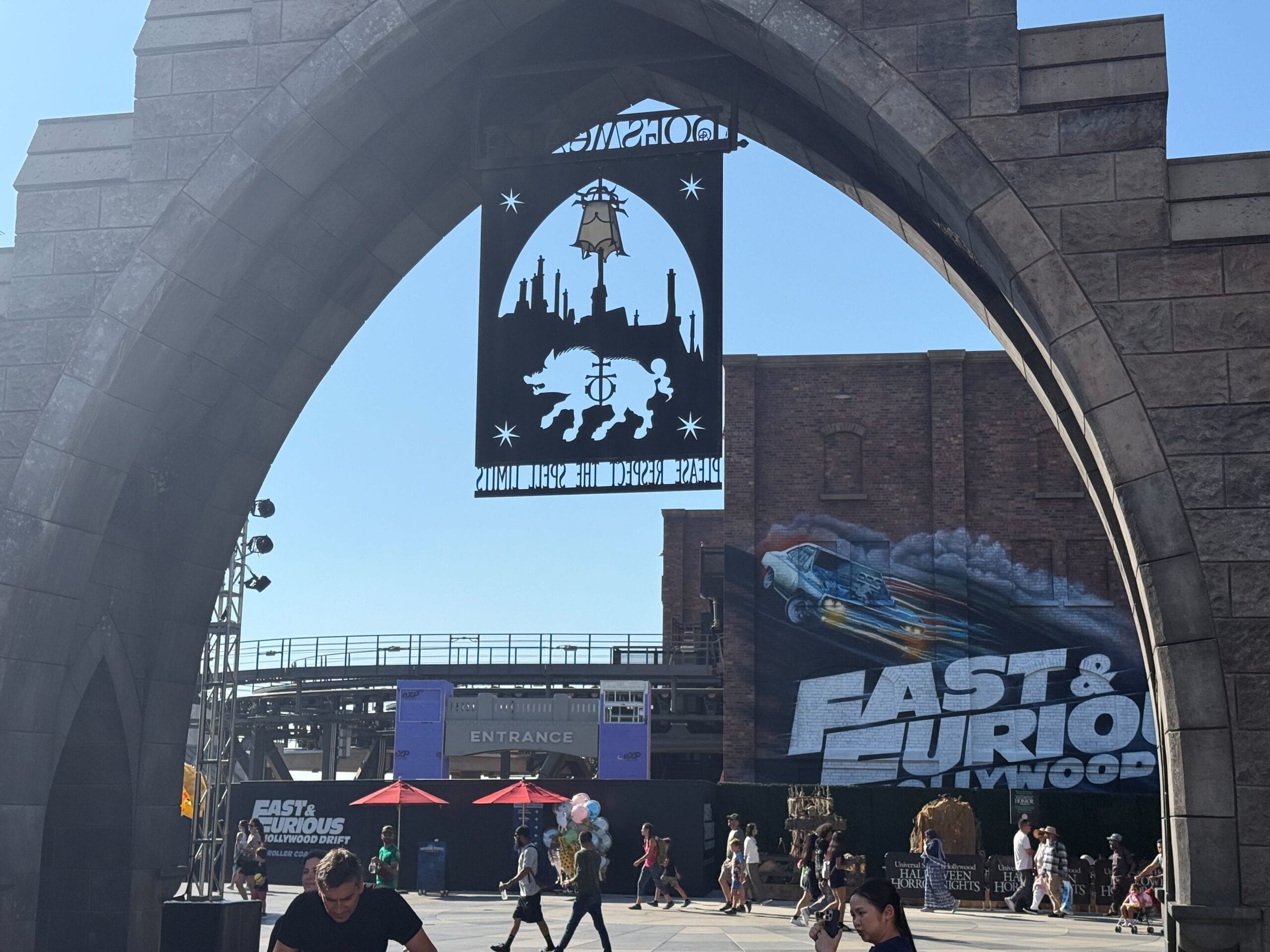 The stone archway to The Wizarding World of Harry Potter – Hogsmeade frames the entrance archway and brick show building for Fast & Furious: Hollywood Drift at Universal Studios Hollywood.