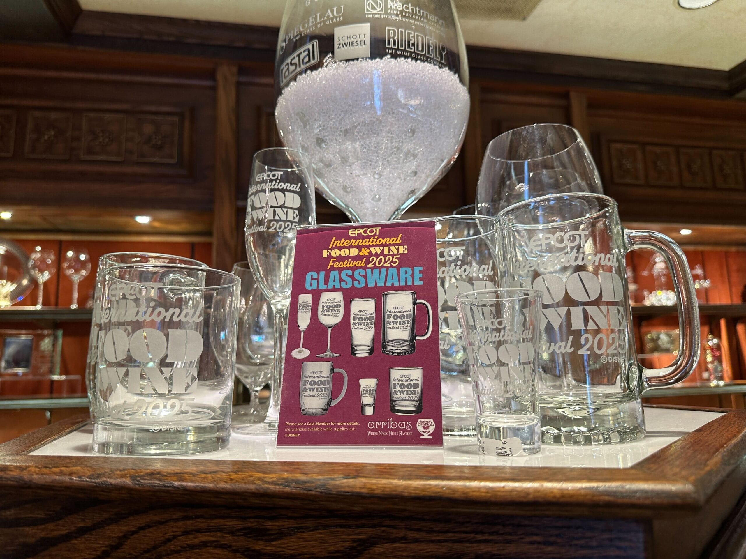EPCOT Food & Wine Festival glassware displayed with a promo card in a wooden cabinet.
