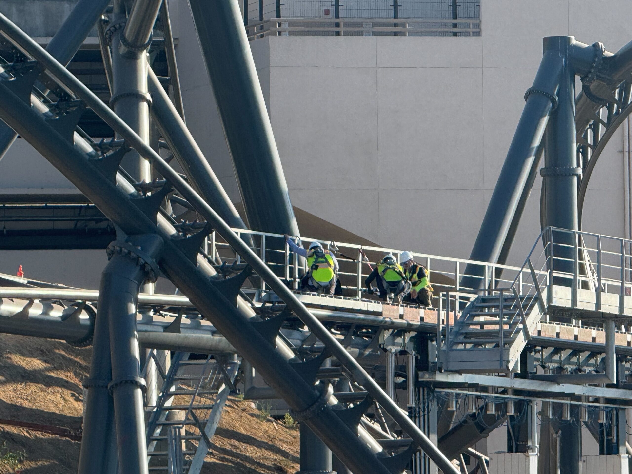 Four construction workers in safety gear crouch on a platform amid the twisting tracks of the Fast & Furious: Hollywood Drift roller coaster at Universal Studios Hollywood.