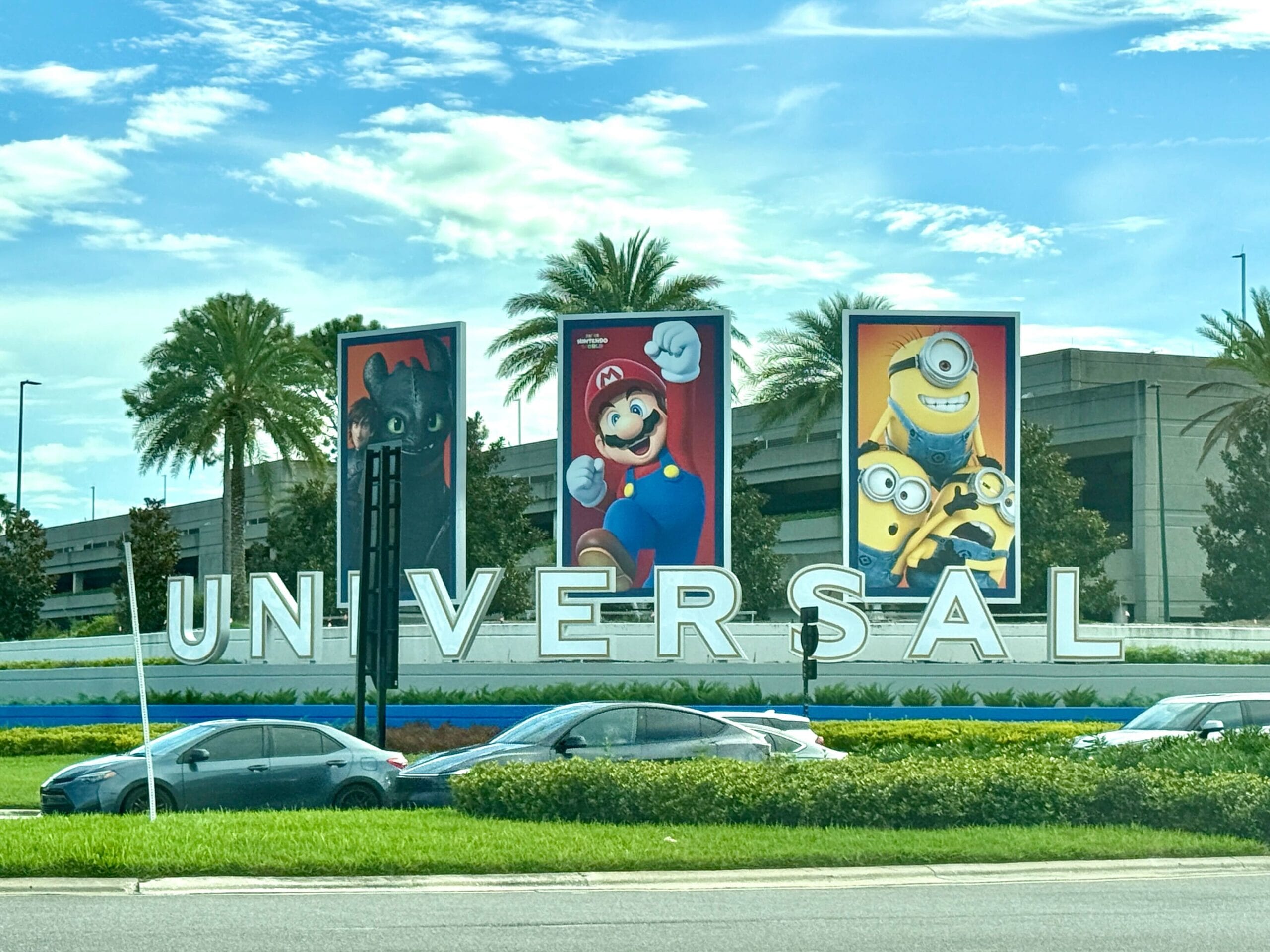 The Universal Studios sign with Entrance Characters banners—Toothless, Mario, Minions—cars passing in front.