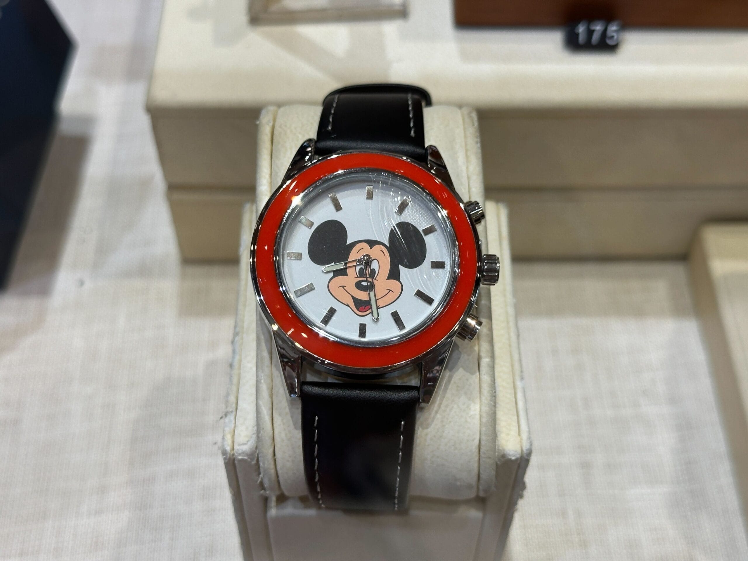 A wristwatch with a red bezel and a Mickey Mouse face design from the 70th Collection, displayed on a white stand.
