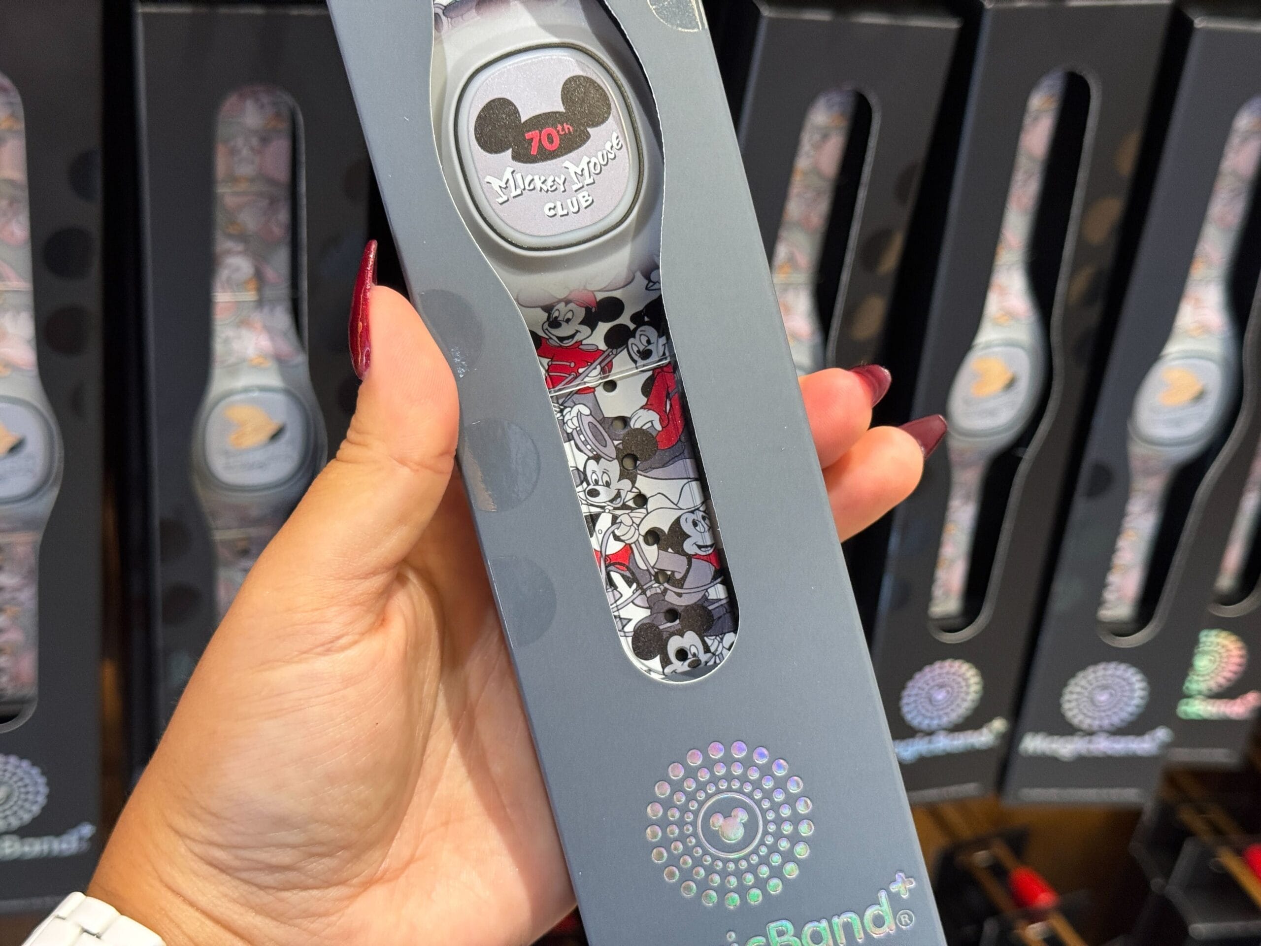 Hand holding a Disney MagicBand+ from the 70th Collection featuring classic Mickey Mouse Club designs in store packaging.