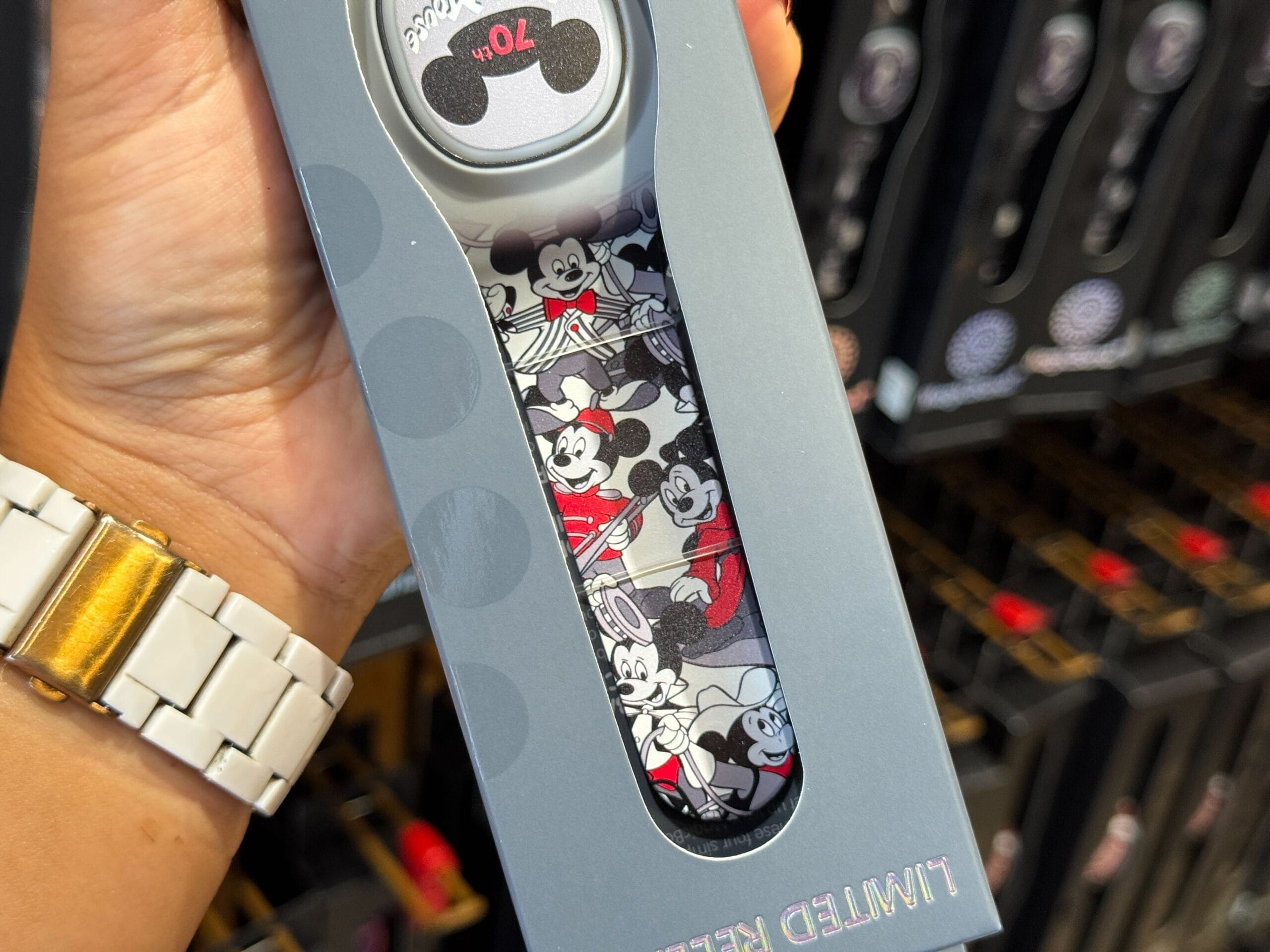 A hand holds a limited edition Disney key from the Mickey Mouse Club 70th Collection in a store display.