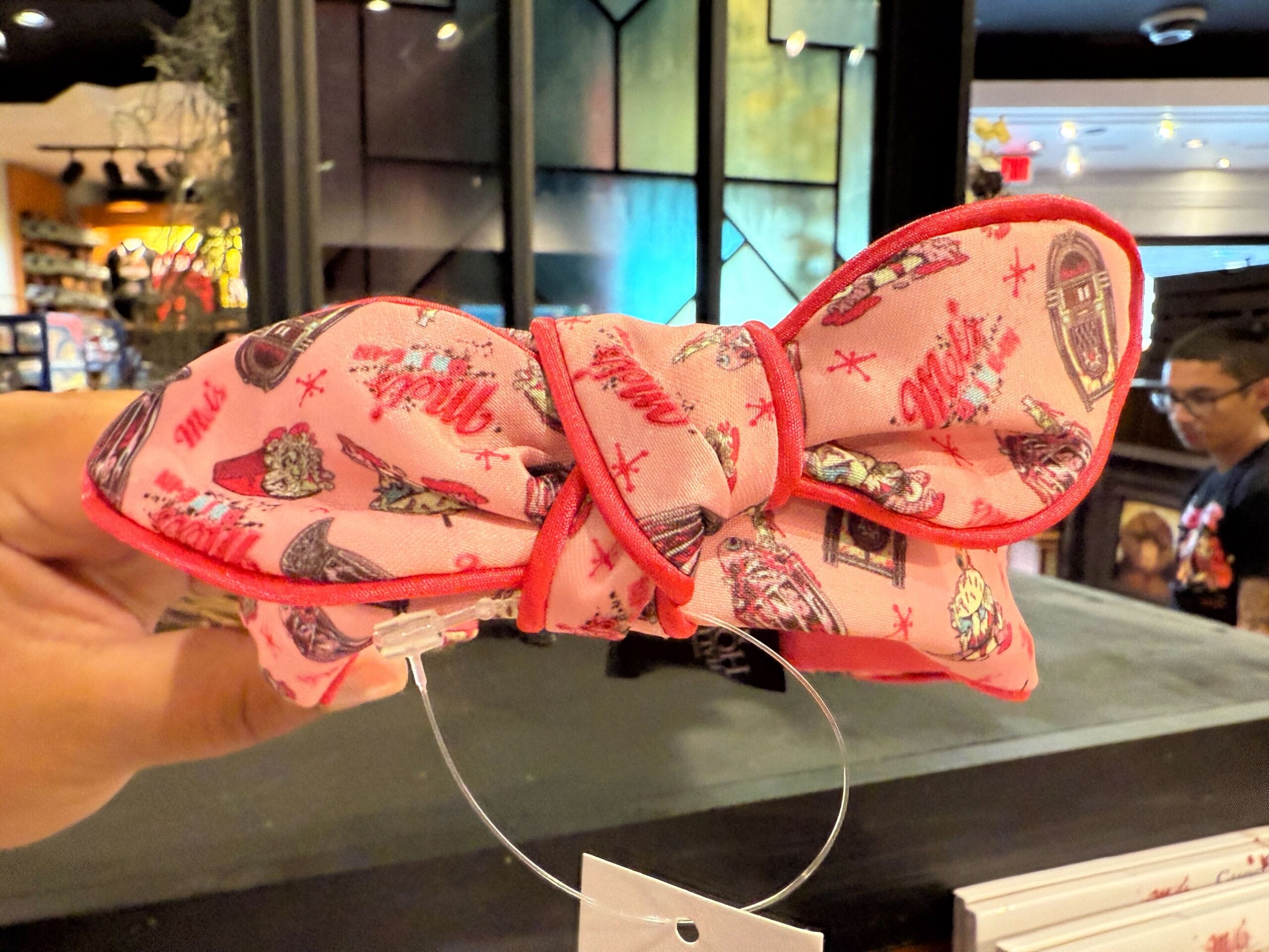 A hand holds a pink Minnie Mouse ear headband with retro food and drink patterns in a store.
