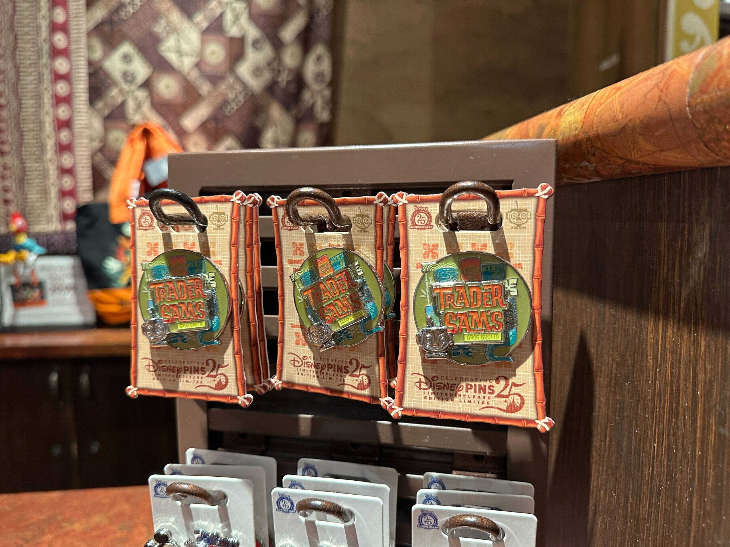 Three Disney’s Trader Sam’s souvenir pins are displayed on a rack inside a themed gift shop.