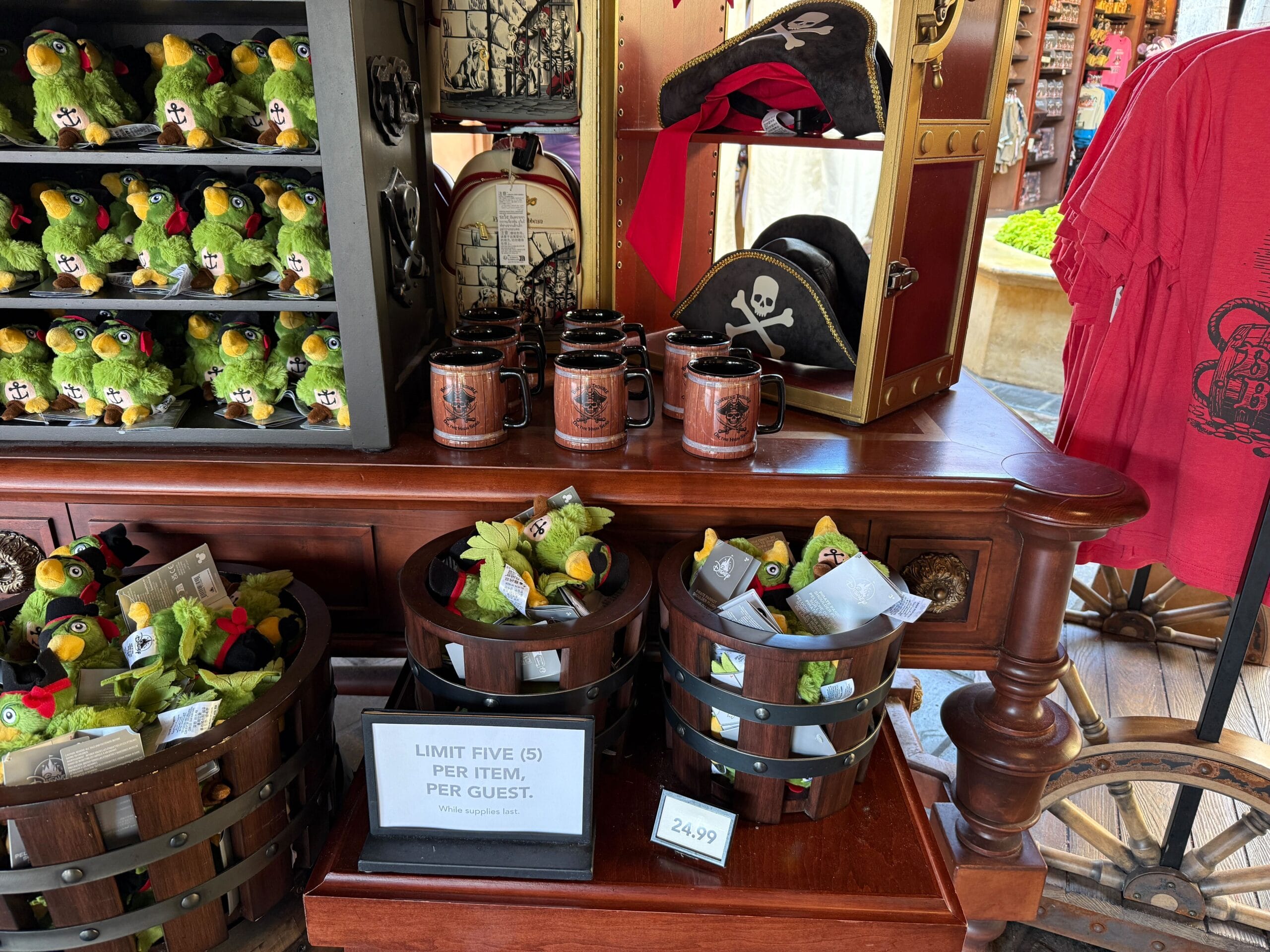 Pirate-themed merchandise, like Pirate Mugs and plush parrots, displayed on a wooden table at Walt Disney World.