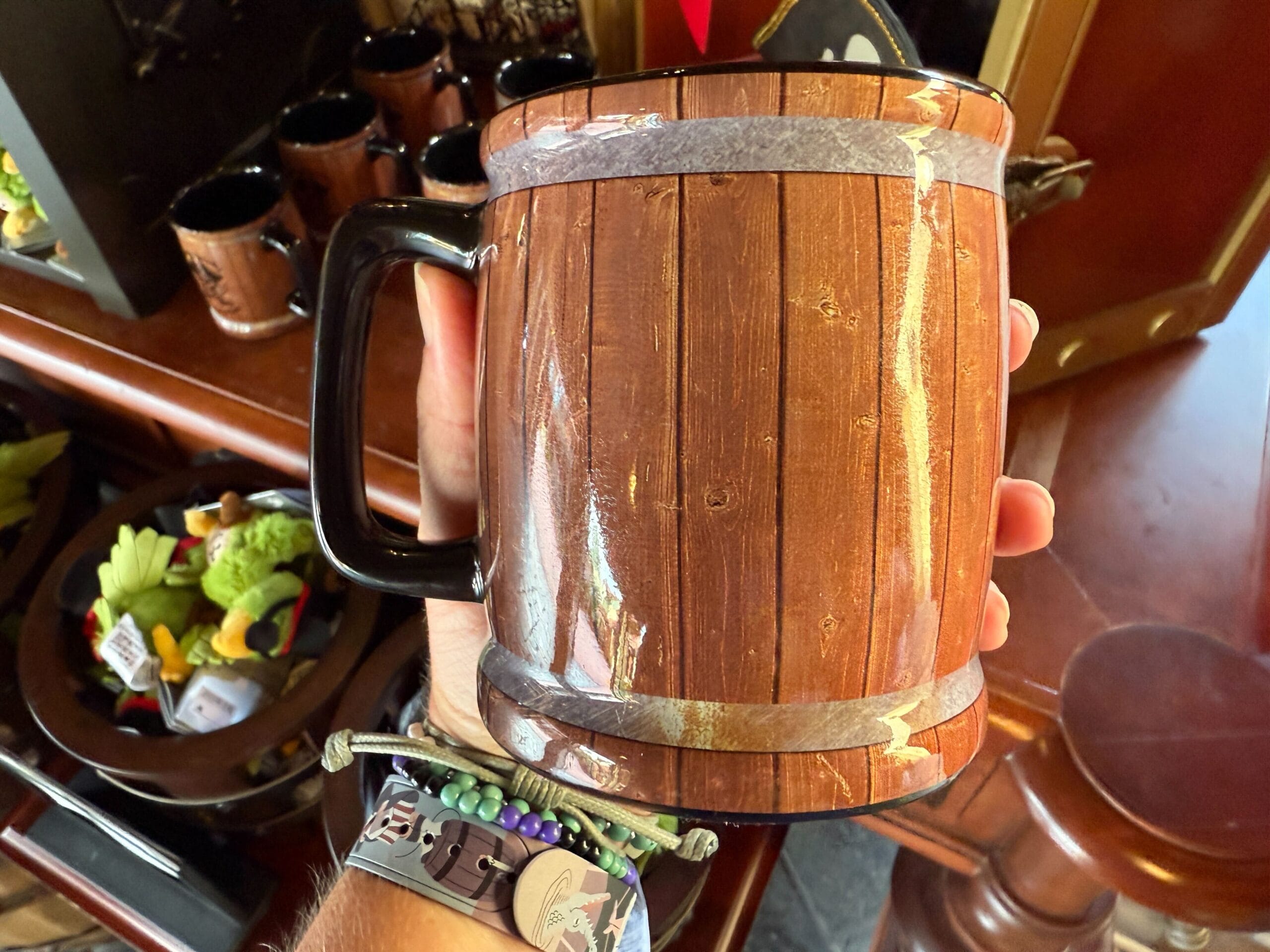 A hand holds a brown barrel-inspired mug with a black handle and plush parrots behind.
