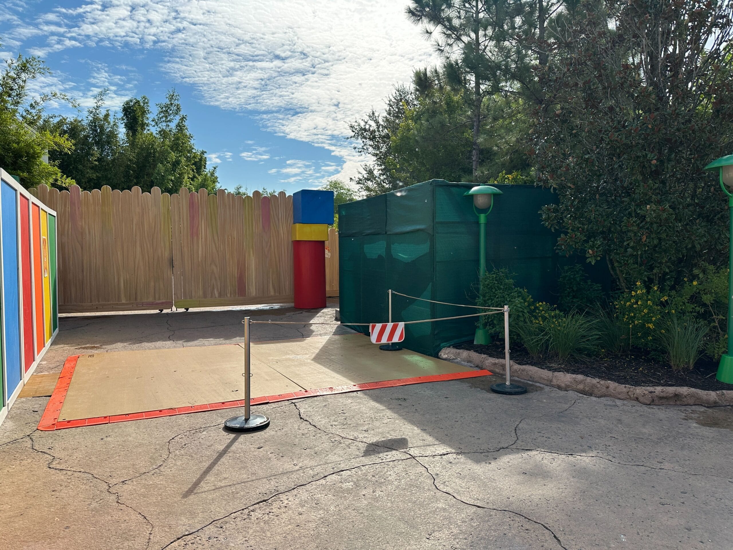 A closed-off outdoor area with construction barriers in Hollywood Studios, under a partly cloudy sky and colorful walls.