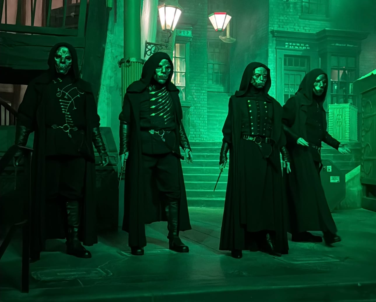 Four people in black hooded costumes stand on a green-tinted street at Halloween Horror Night 2025.