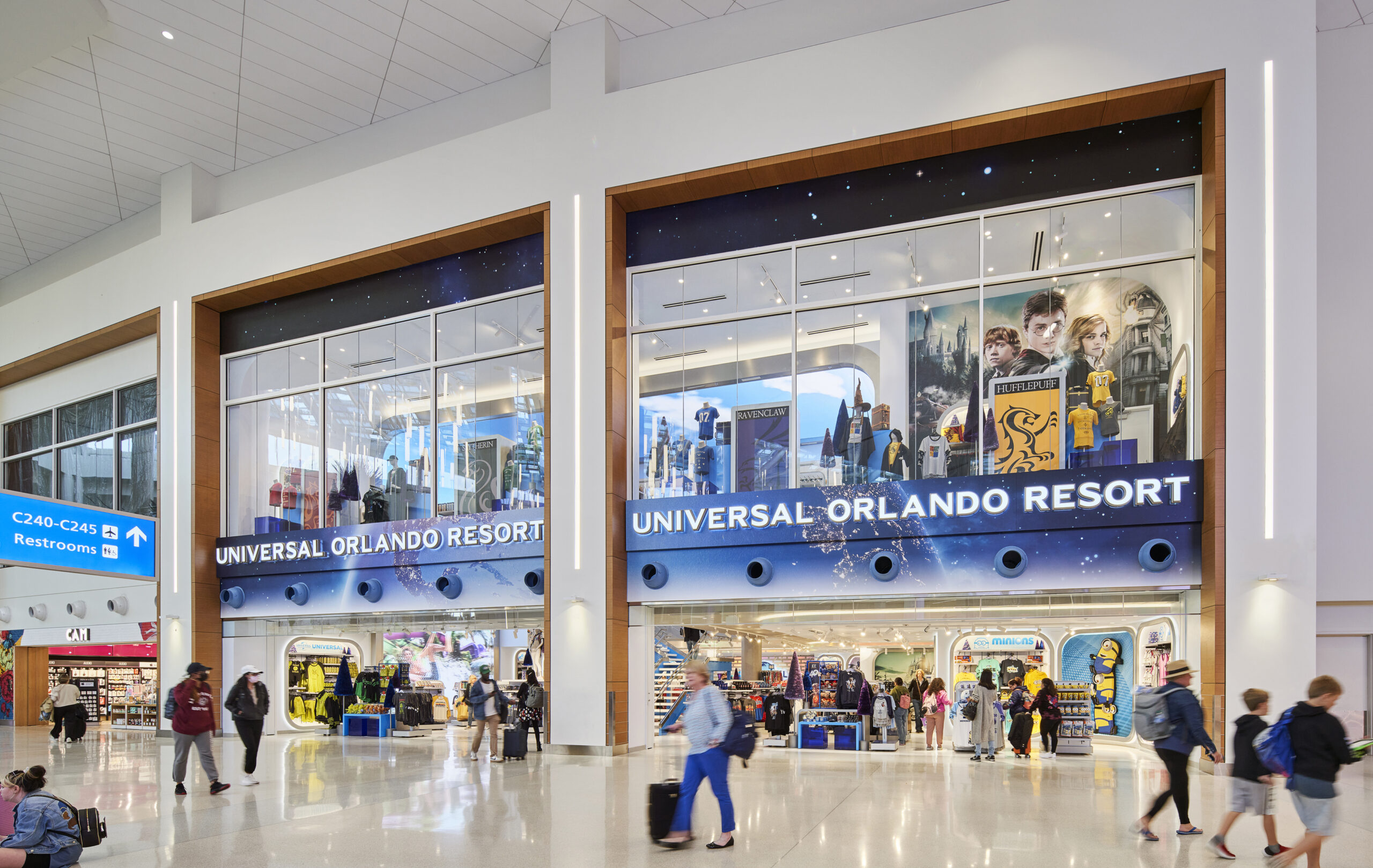 Travelers walk past a Universal Orlando Resort store at Orlando International Airport, featuring movie-themed displays.