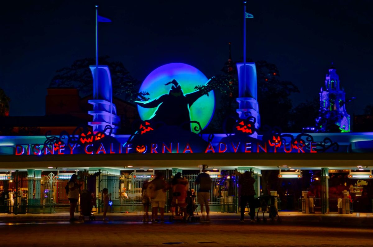 Disney California Adventure entrance at night, glowing for Oogie Boogie Bash 2025 with Halloween lights and a moon featuring Oogie Boogie.