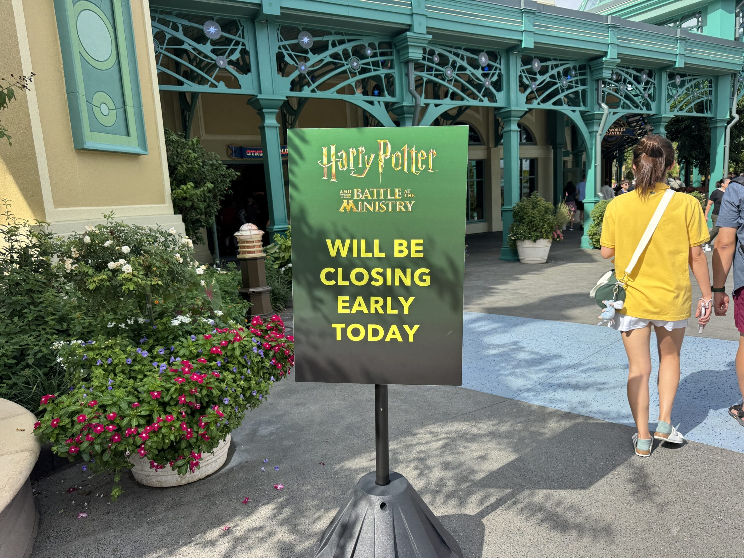 Sign reads: “Harry Potter: Battle for the Ministry at Epic Universe will be closing early today” outside a green and yellow building.