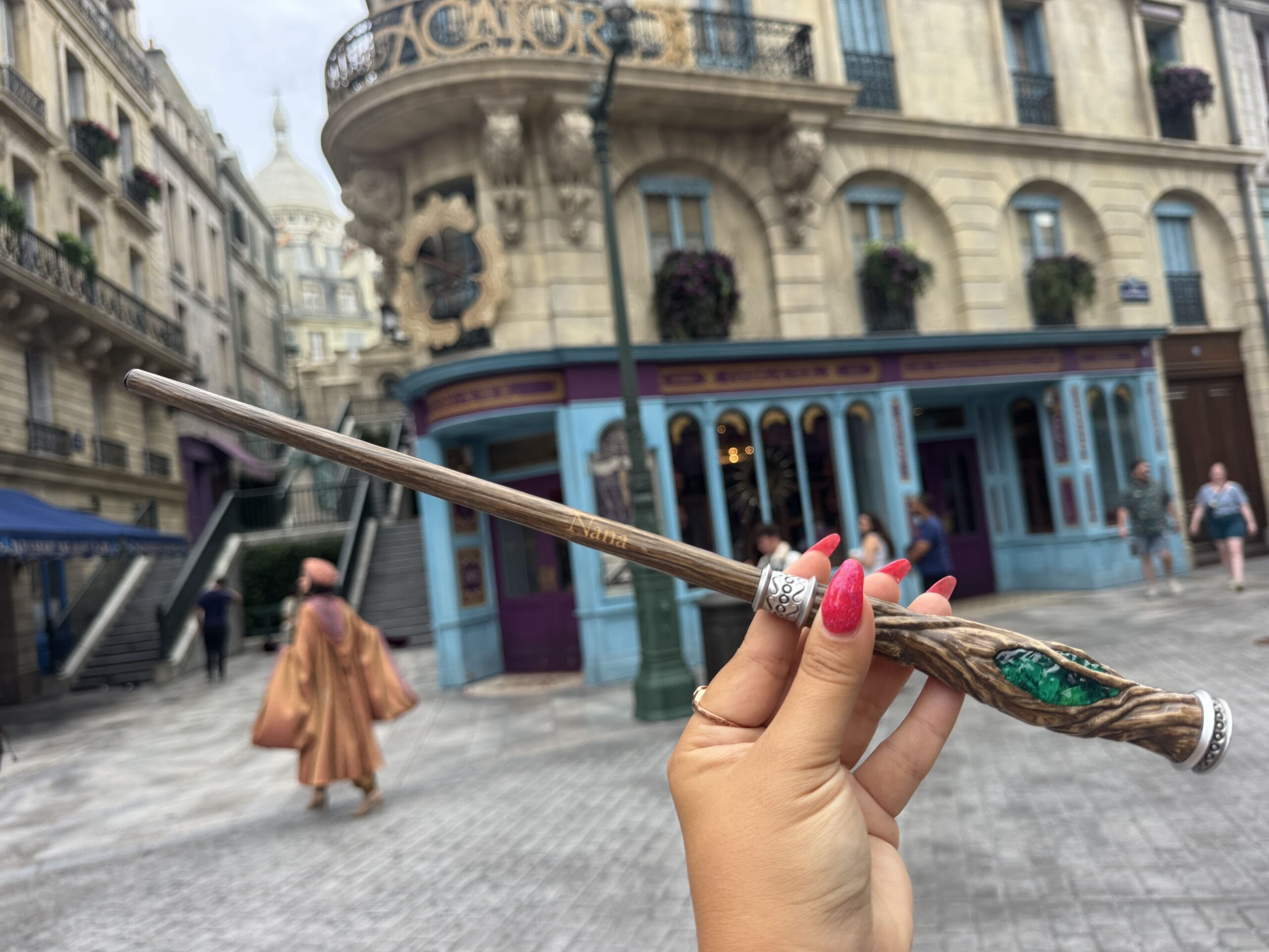 A hand with red nails holds a wand, ready to personalize your wand on a cobblestone street in Epic Universe.