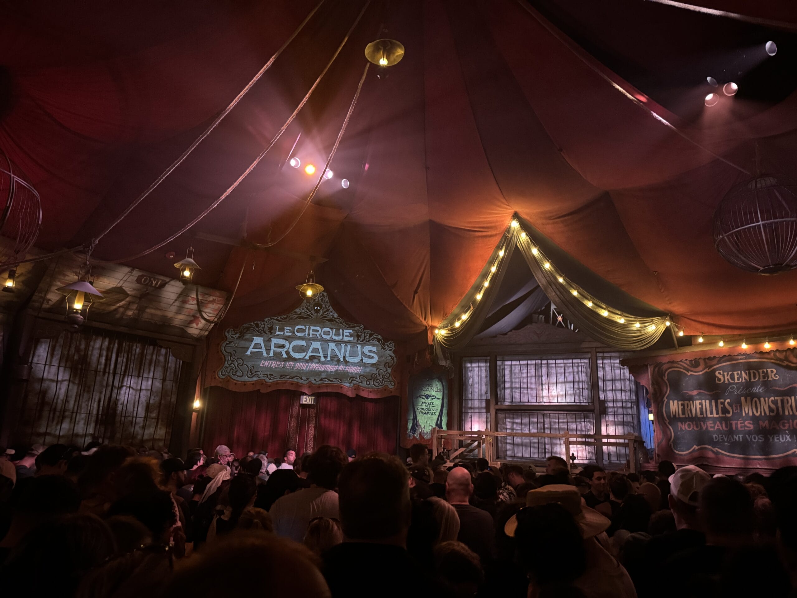A crowd gathers under a red circus tent at Epic Universe, with signs reading "Le Cirque Arcanus" and "Skender Merveilles et Monstres.
