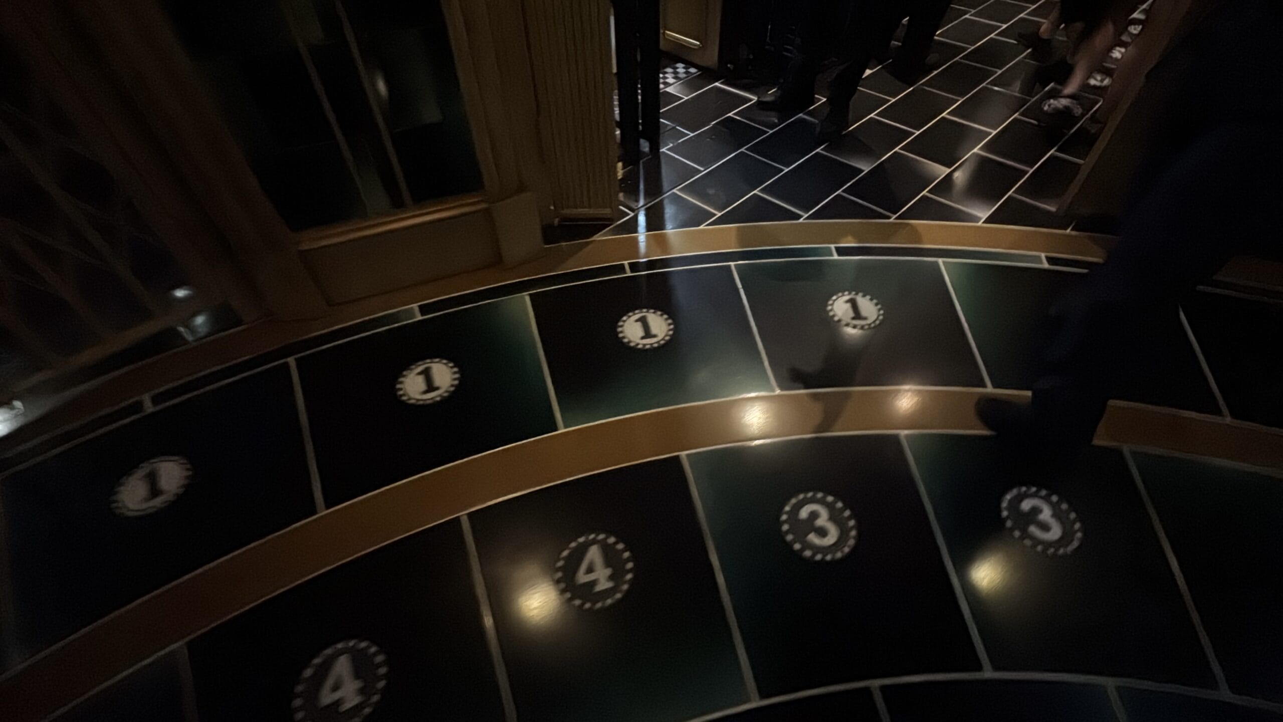 People walk on black tiles with numbered circles at Epic Universe in a dimly lit indoor setting.
