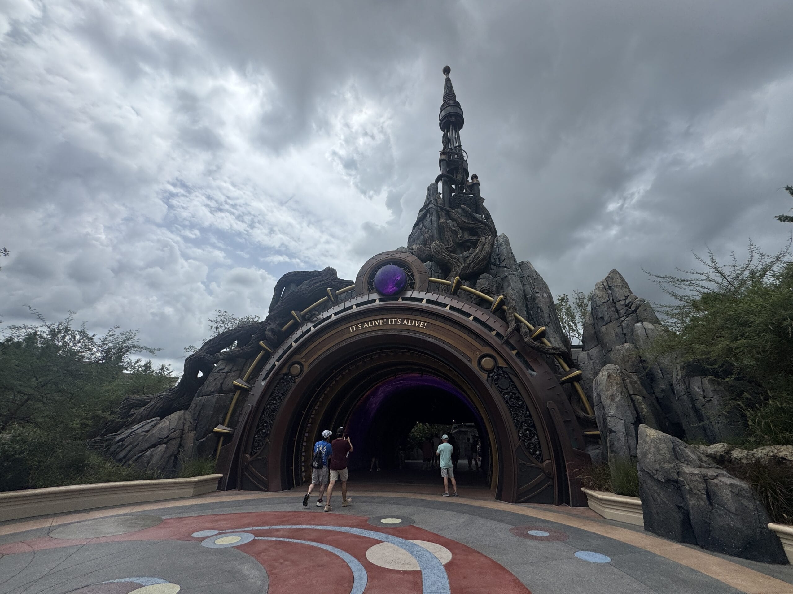 People walk toward a fantasy-themed tunnel at Epic Universe, a perfect spot for rainy day activities beneath cloudy skies.