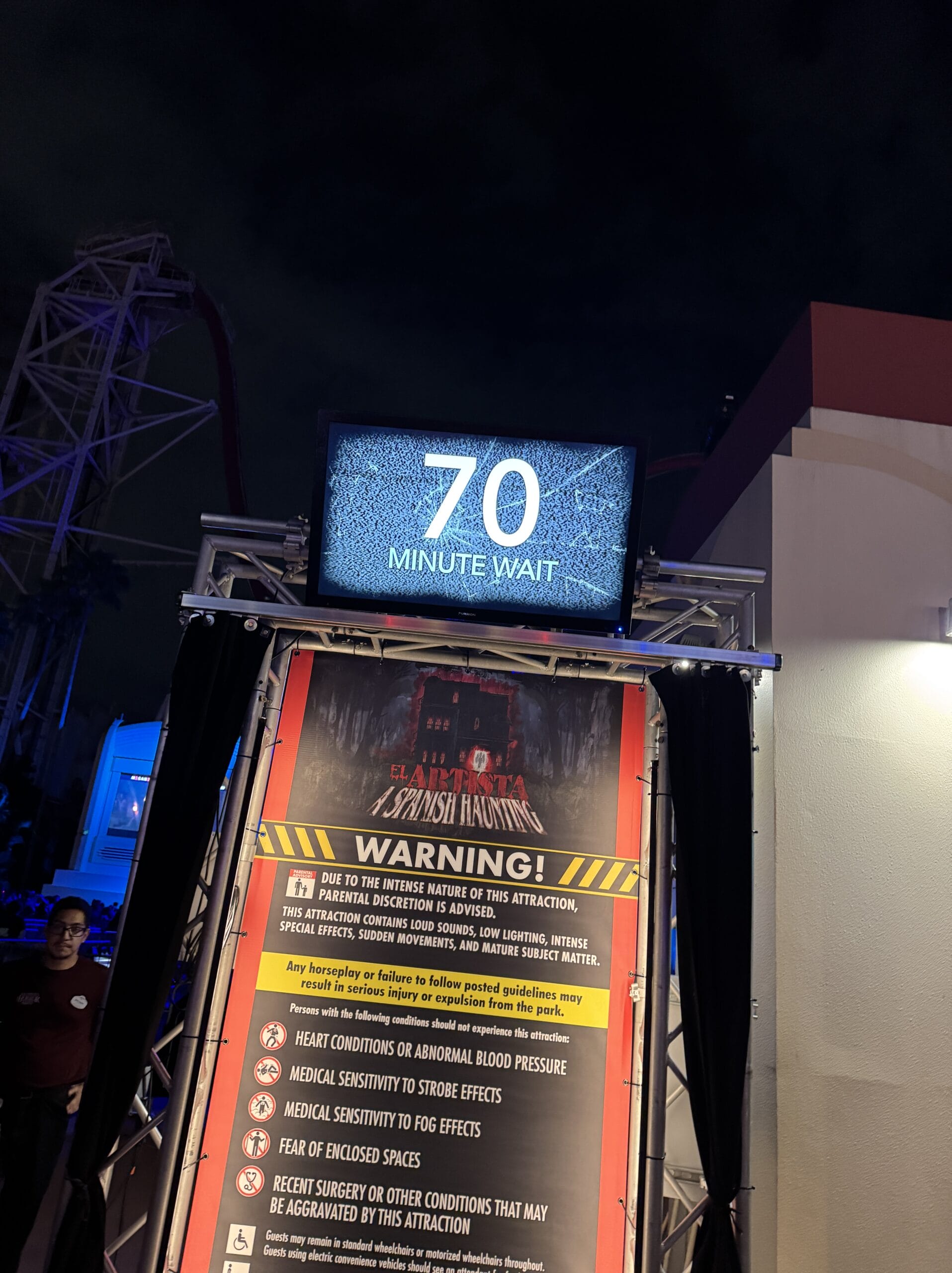 A digital sign displays "70 minute wait" at a Halloween Horror Night 2025 attraction entrance after dark.