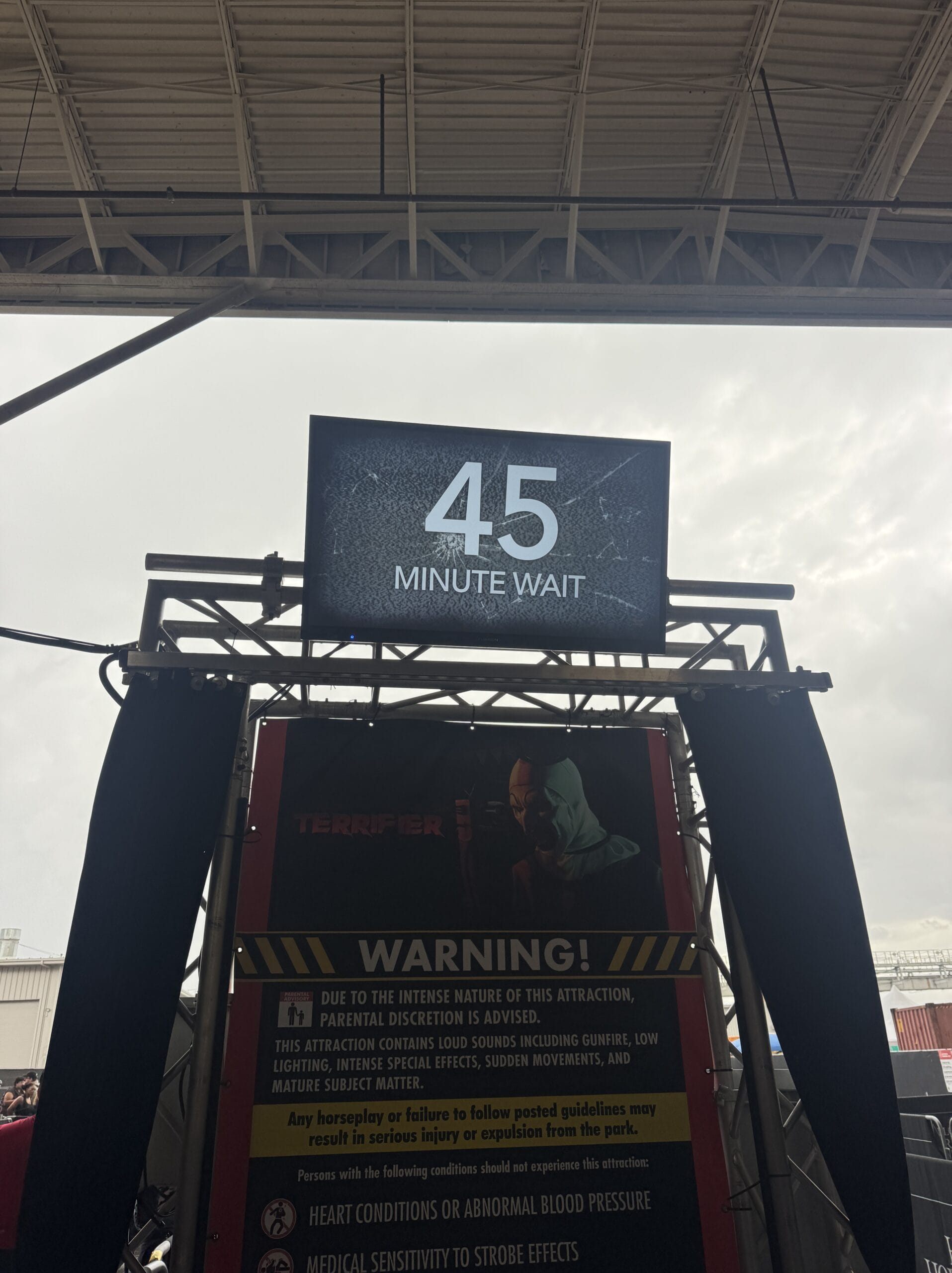 A digital sign reads "45 minute wait" above a Halloween Horror Night warning poster at the haunted attraction entrance.