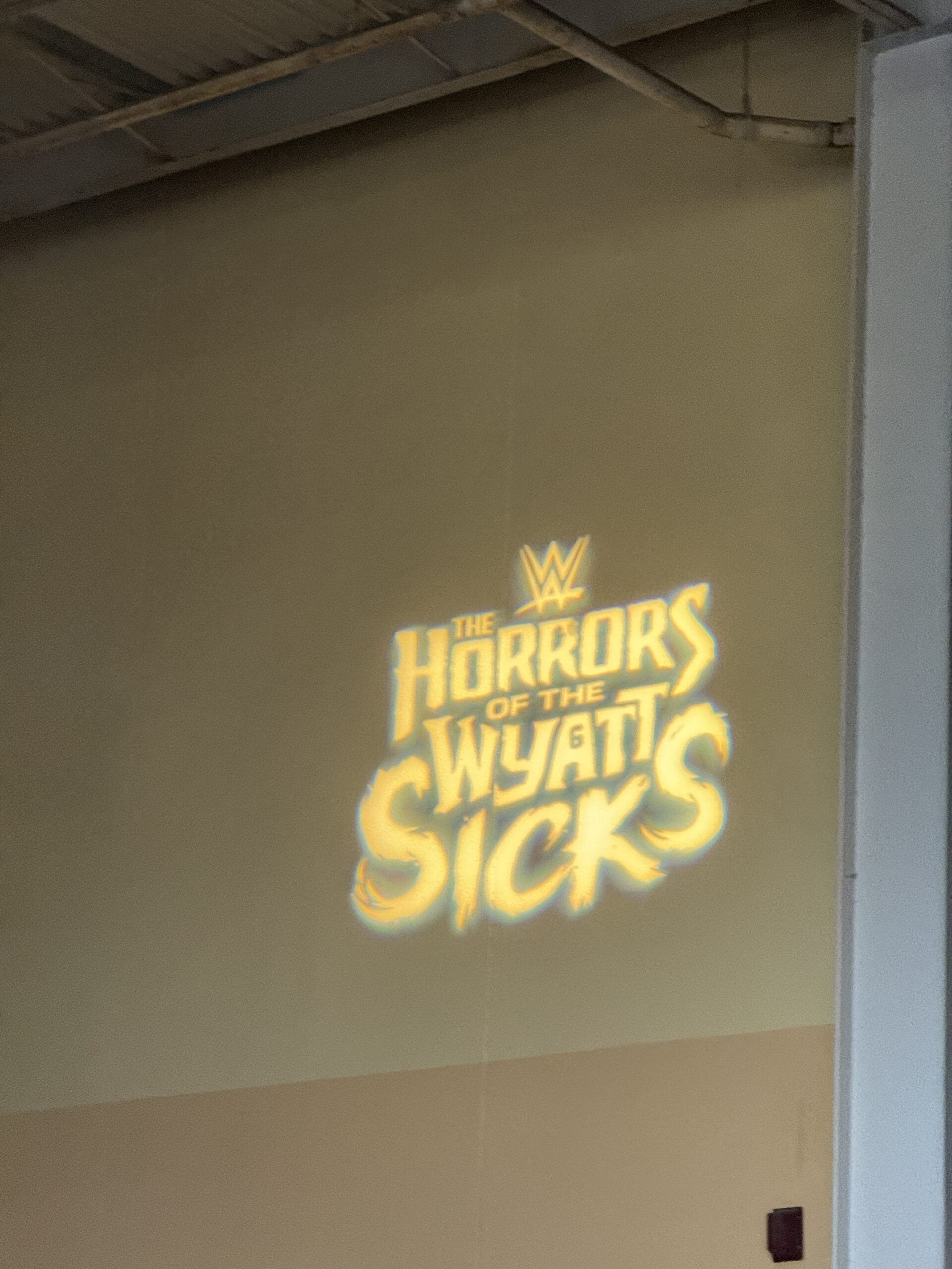 A projected yellow sign on the wall reads "WWE The Horrors of the Wyatt Sicks" at Halloween Horror Night 34.