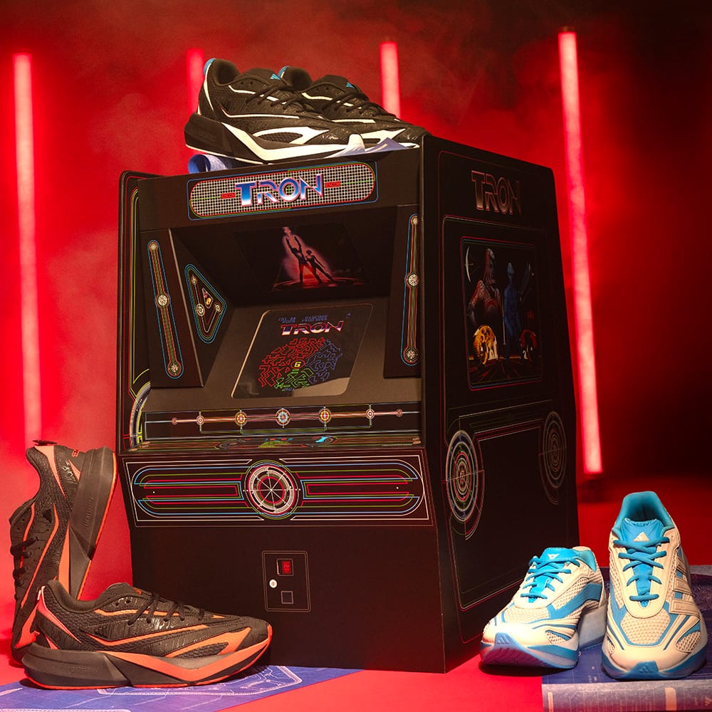 TRON-themed arcade cabinet box with three pairs of Adidas TRON: Ares Lightblaze sneakers in black and red, black and white, and white and blue colorways.
