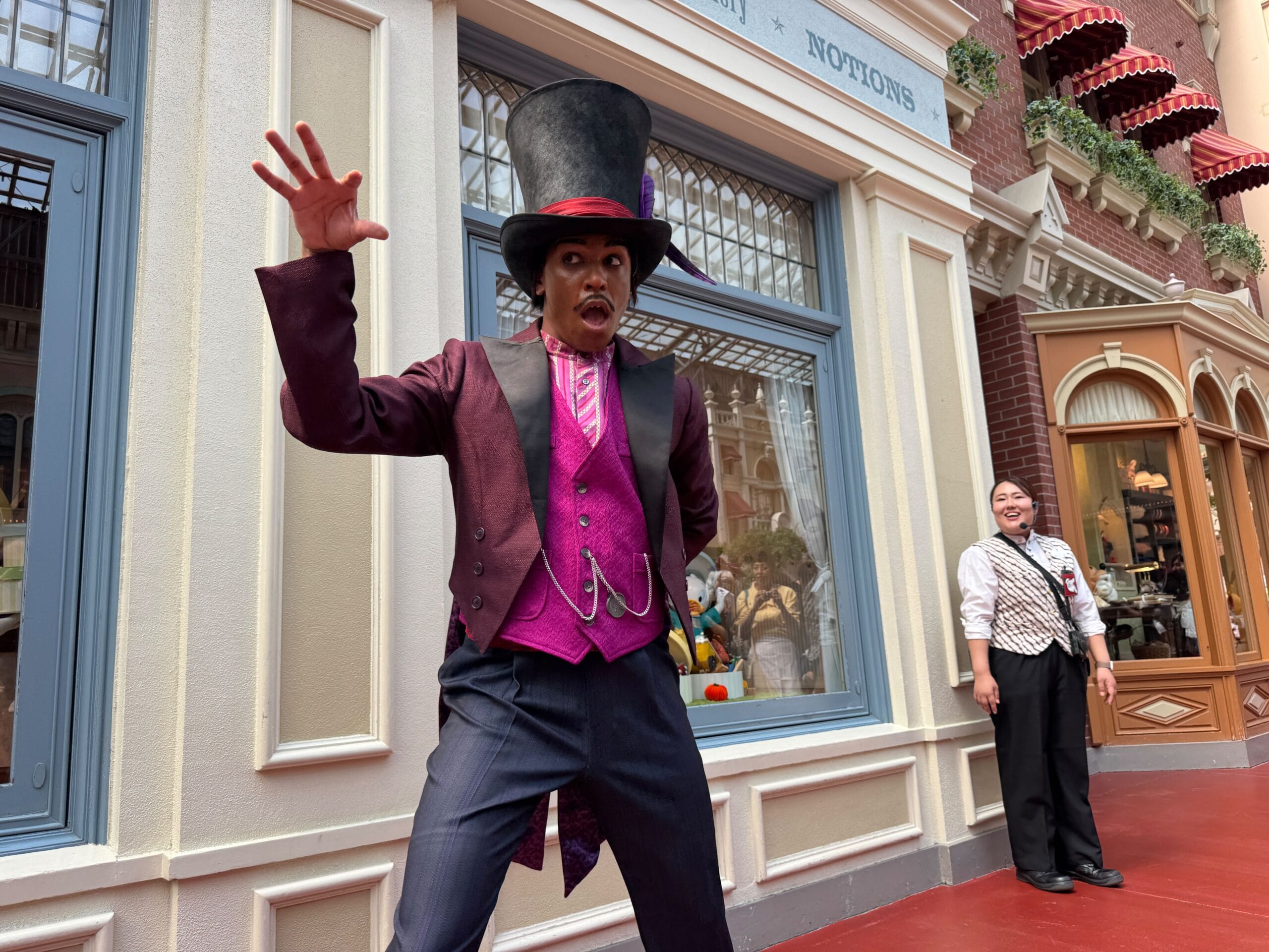 A performer in a Dr. Facilier costume poses energetically on a city street, while a smiling staff member stands nearby.