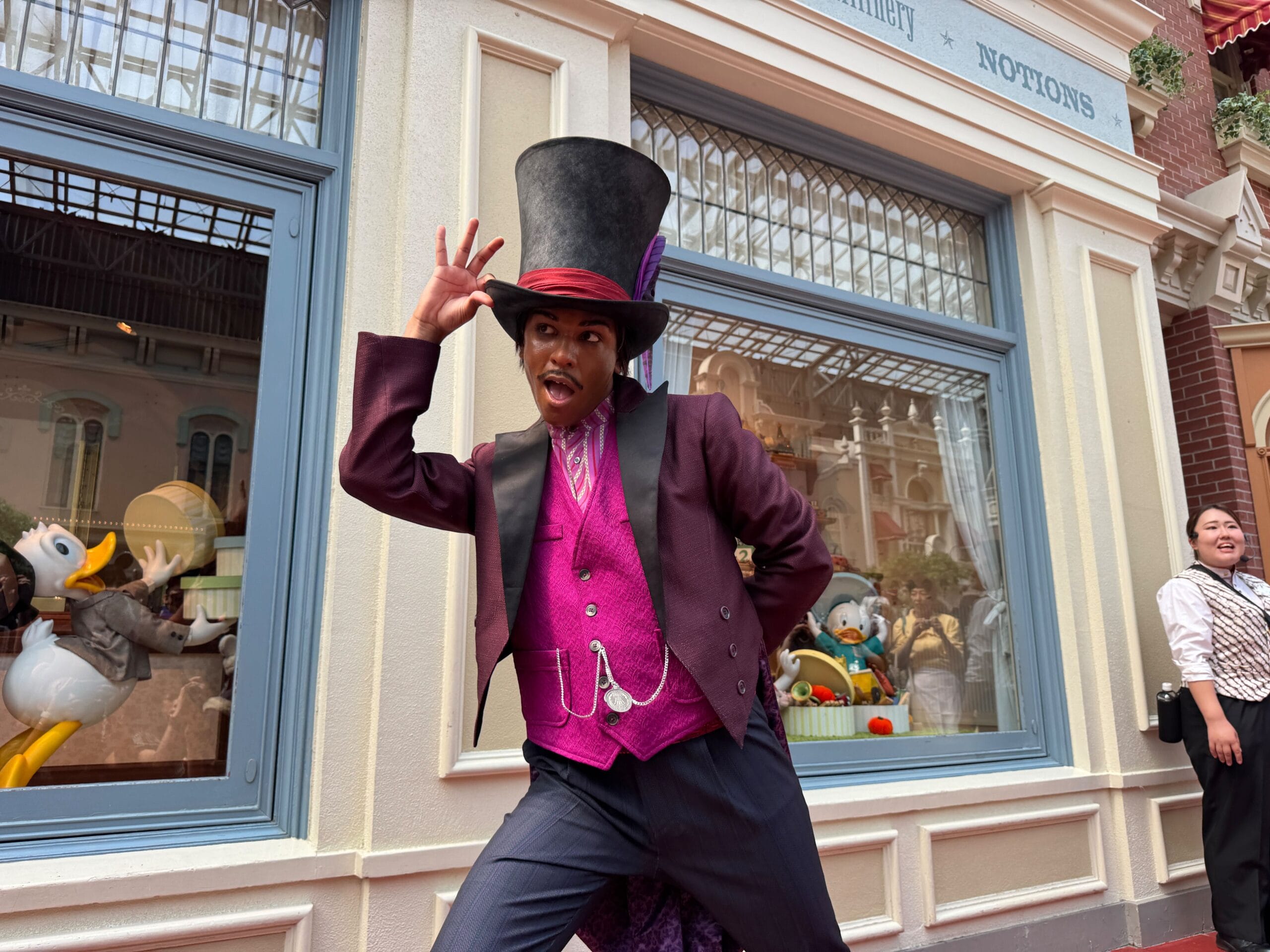A performer in a Dr. Facilier costume poses playfully outside a Tokyo Disneyland shop with Disney figures in the window.