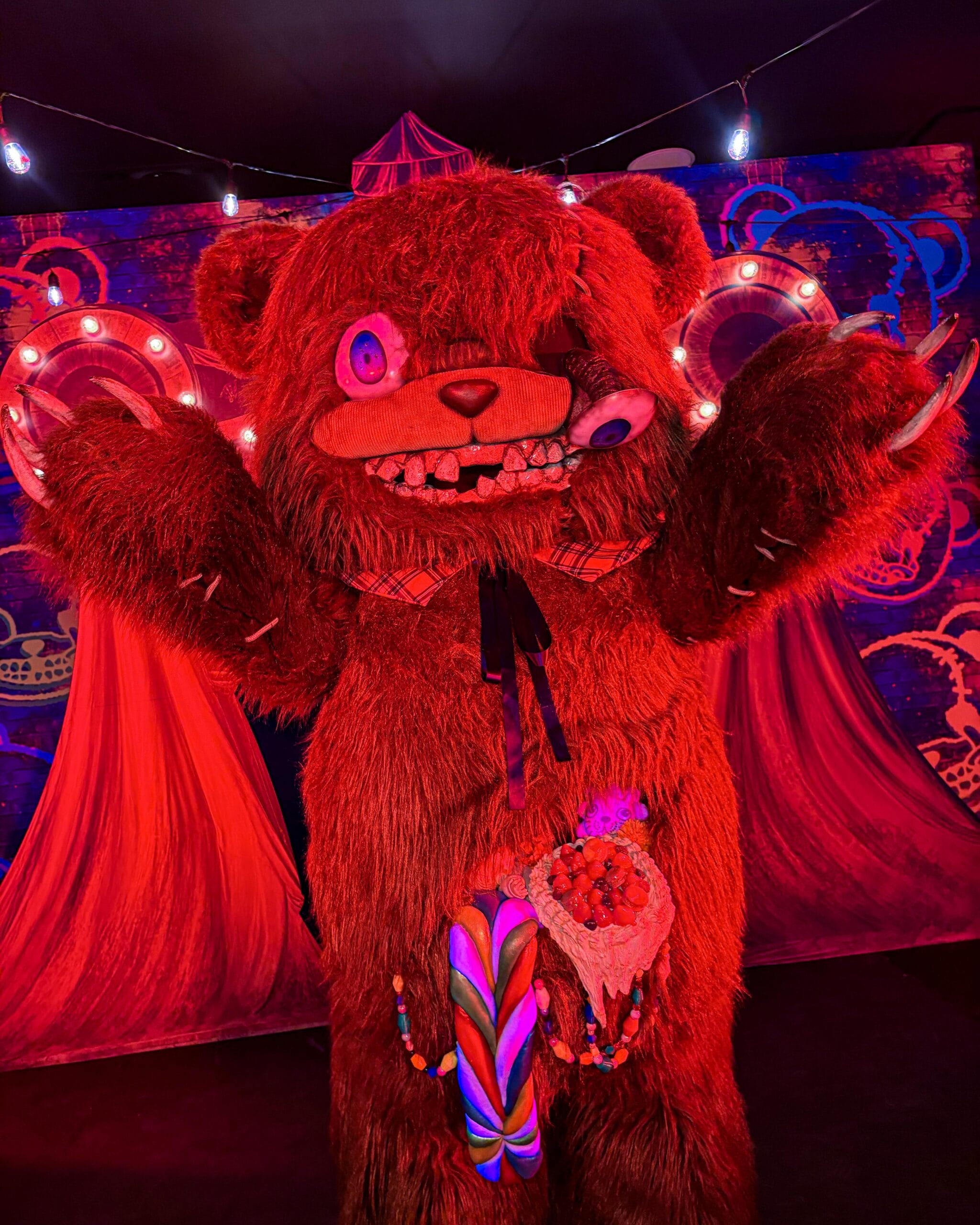 A person in a scary, red HamiKuma bear costume with glowing eyes stands under string lights in Japan.