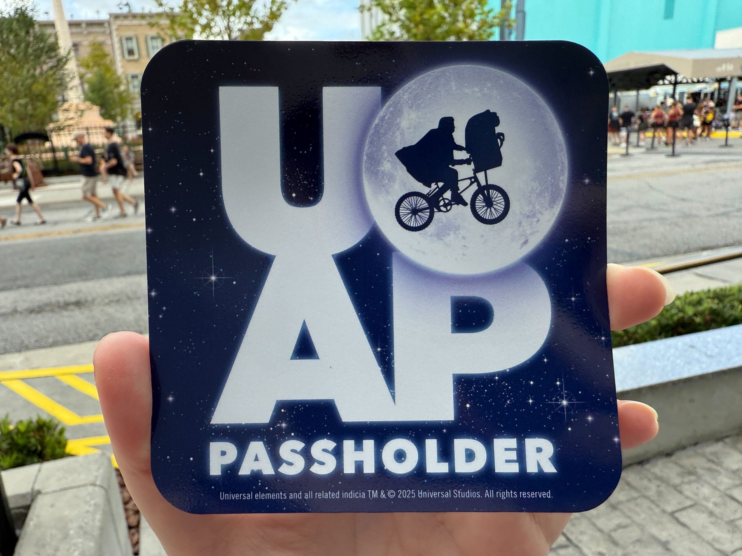 A hand holds a "UOAP Passholder" sign with E.T. biking past the moon—perfect for your 9/11/25 Daily Recap.