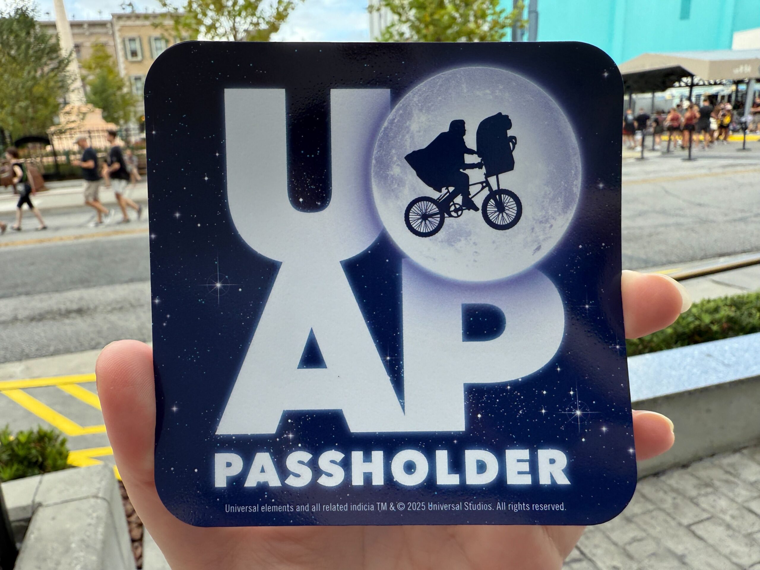 A hand holds a "UOAP Passholder" sign with E.T. Magnet art, celebrating Universal Orlando Annual Passholders.