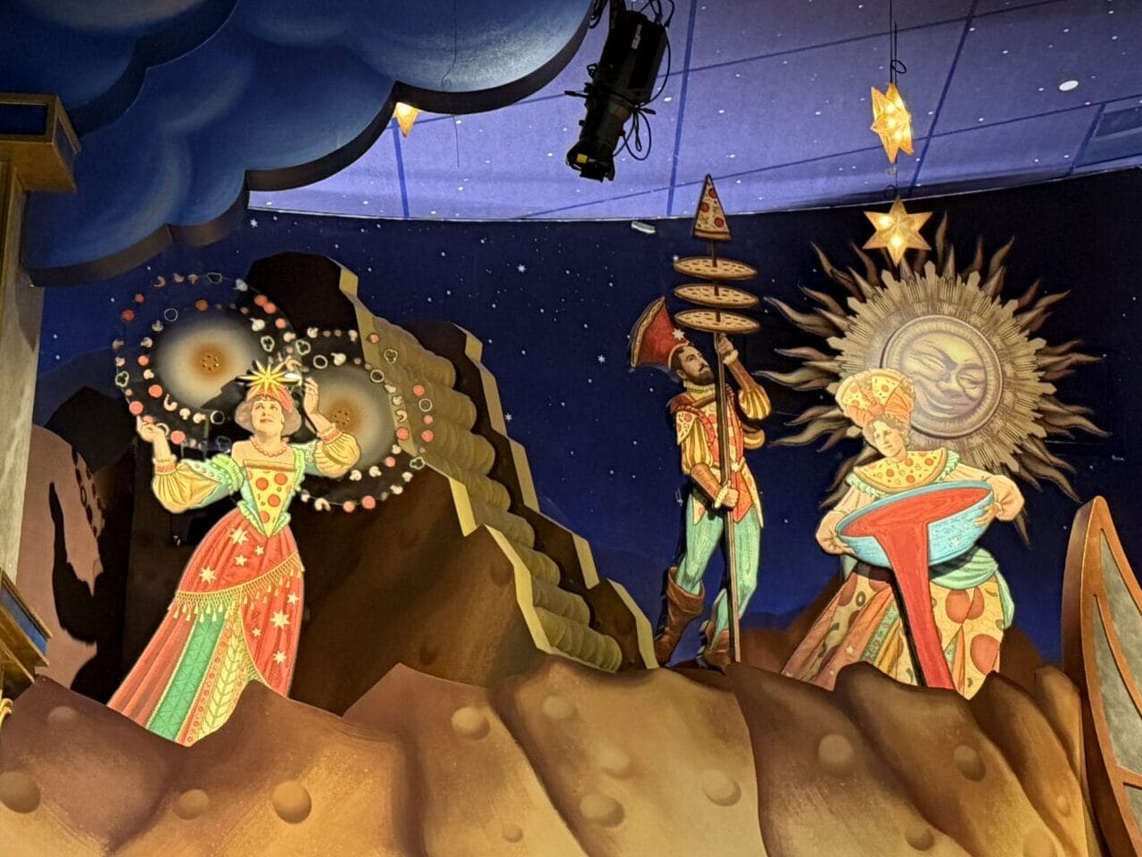 Colorful mural with celestial figures, starry sky, and a large red rocket in Epic Universe’s whimsical, fantasy setting.