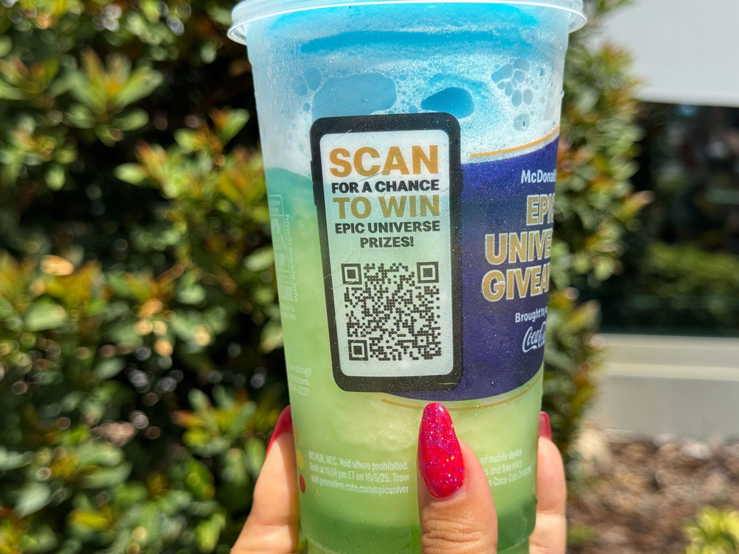 A hand with red nails holds a McDonald's slush cup featuring a QR code for a prize giveaway.