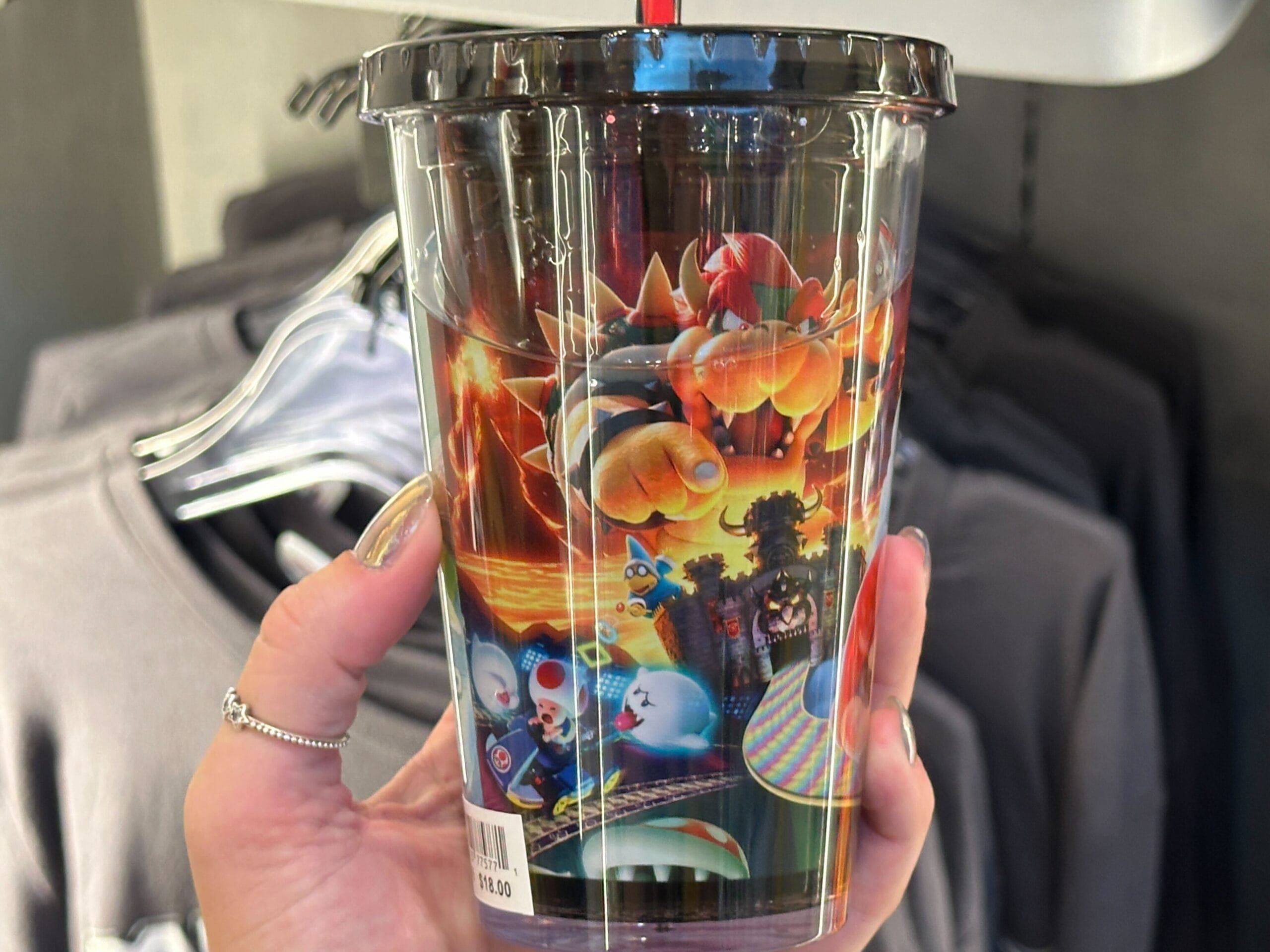 A hand holds a plastic cup featuring colorful Super Mario villains, part of Epic Universe's Mario Motors merchandise line.