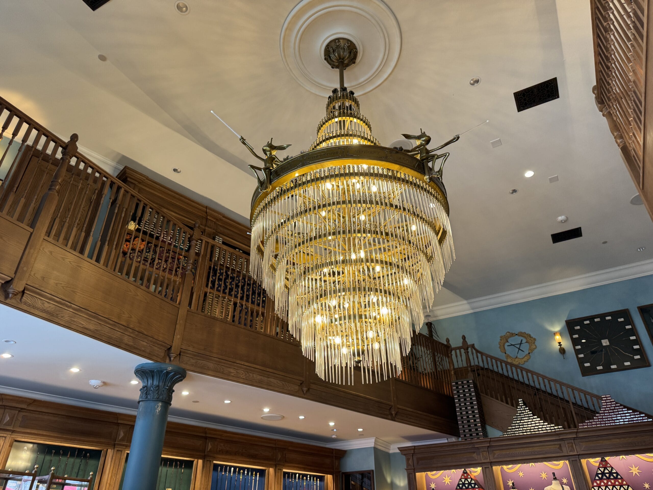 A large chandelier with unicorns, inspired by Cosme Acajor Baguettes Magique, hangs in an elegant, wood-paneled room.