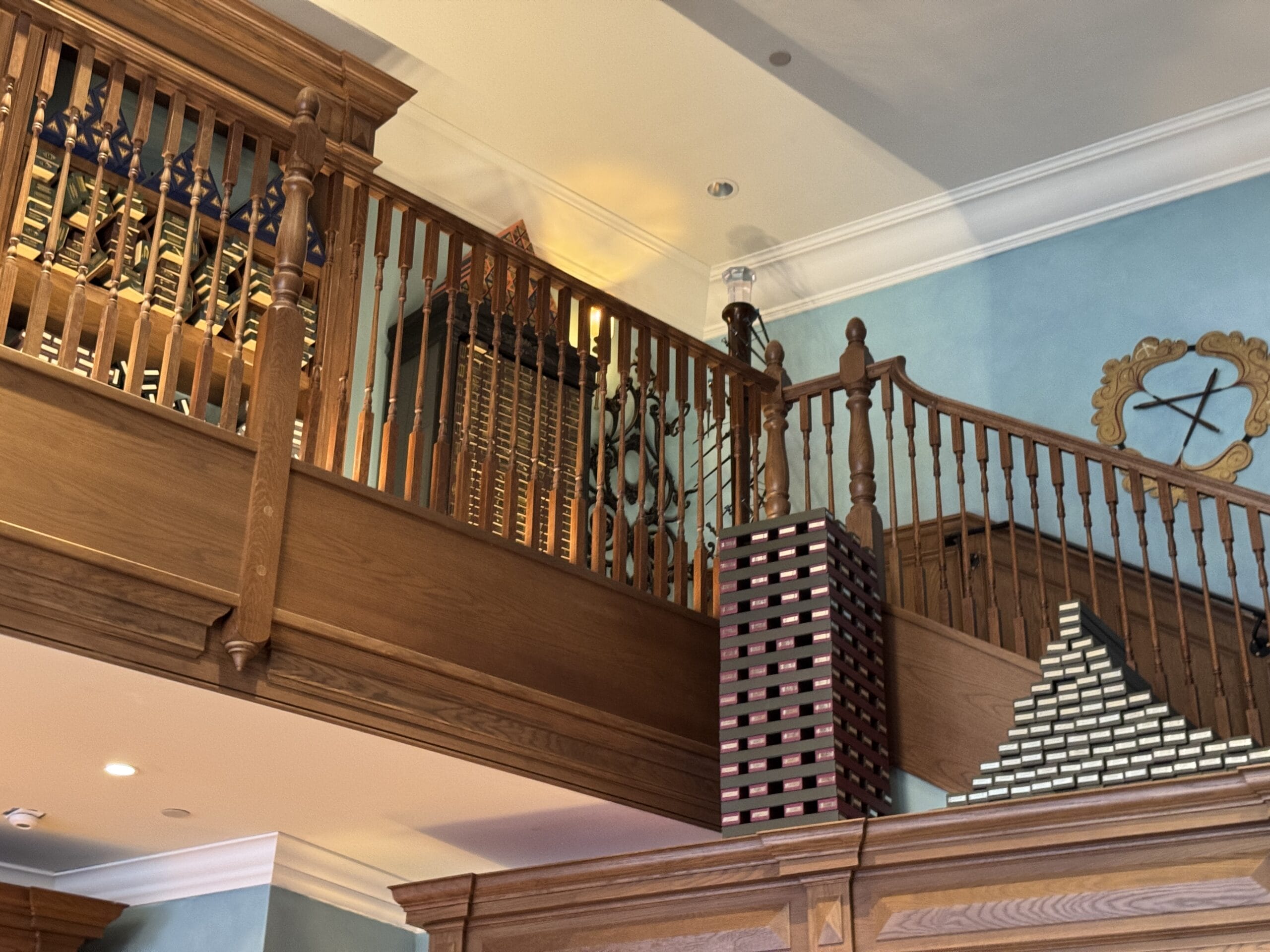A wooden staircase with Cosme Acajor railing in a blue room, stacked books, and geometric wall art.
