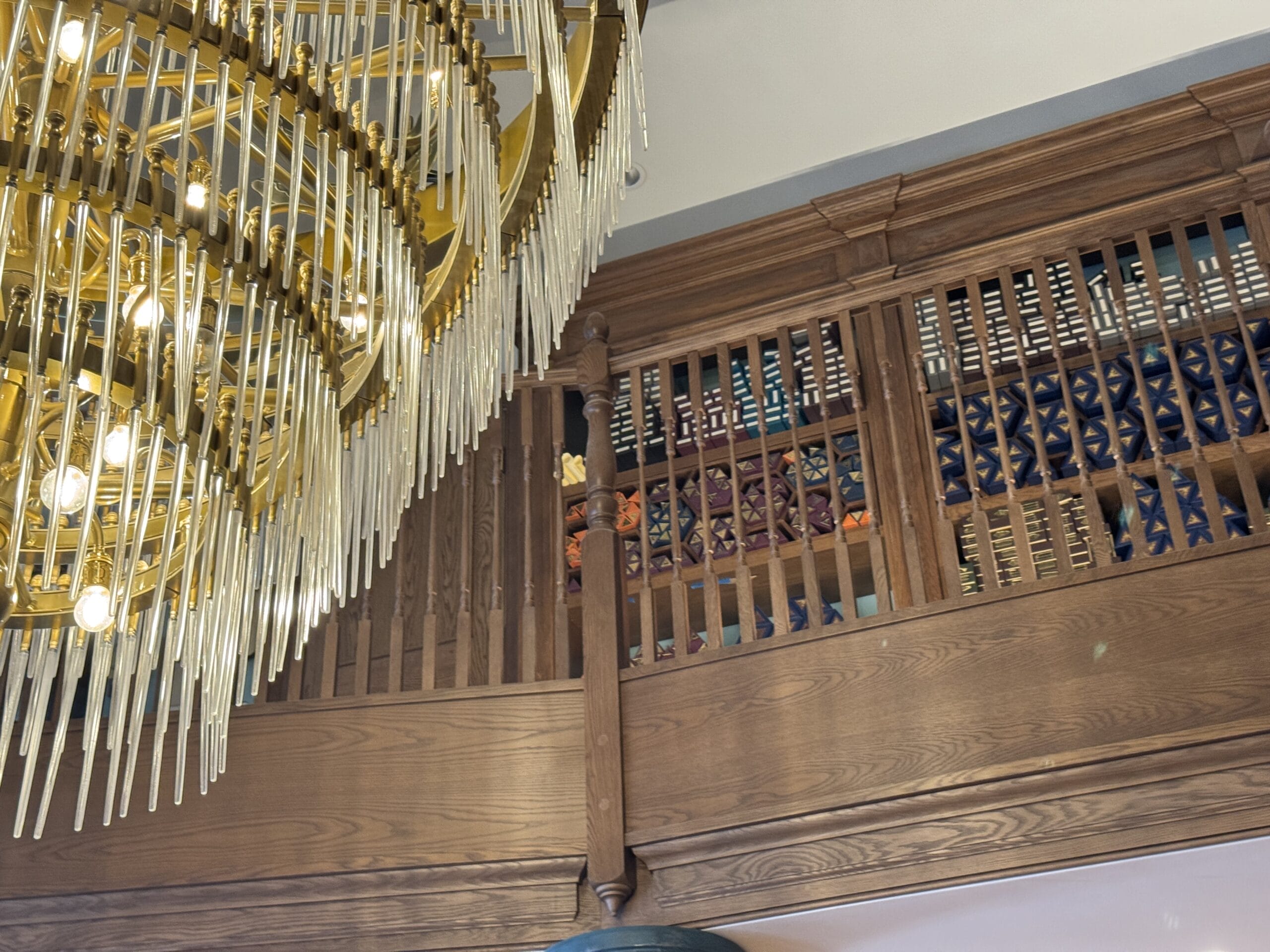 Large chandelier with hanging crystals beside Cosme Acajor Baguettes Magique on a wooden balcony behind a railing.