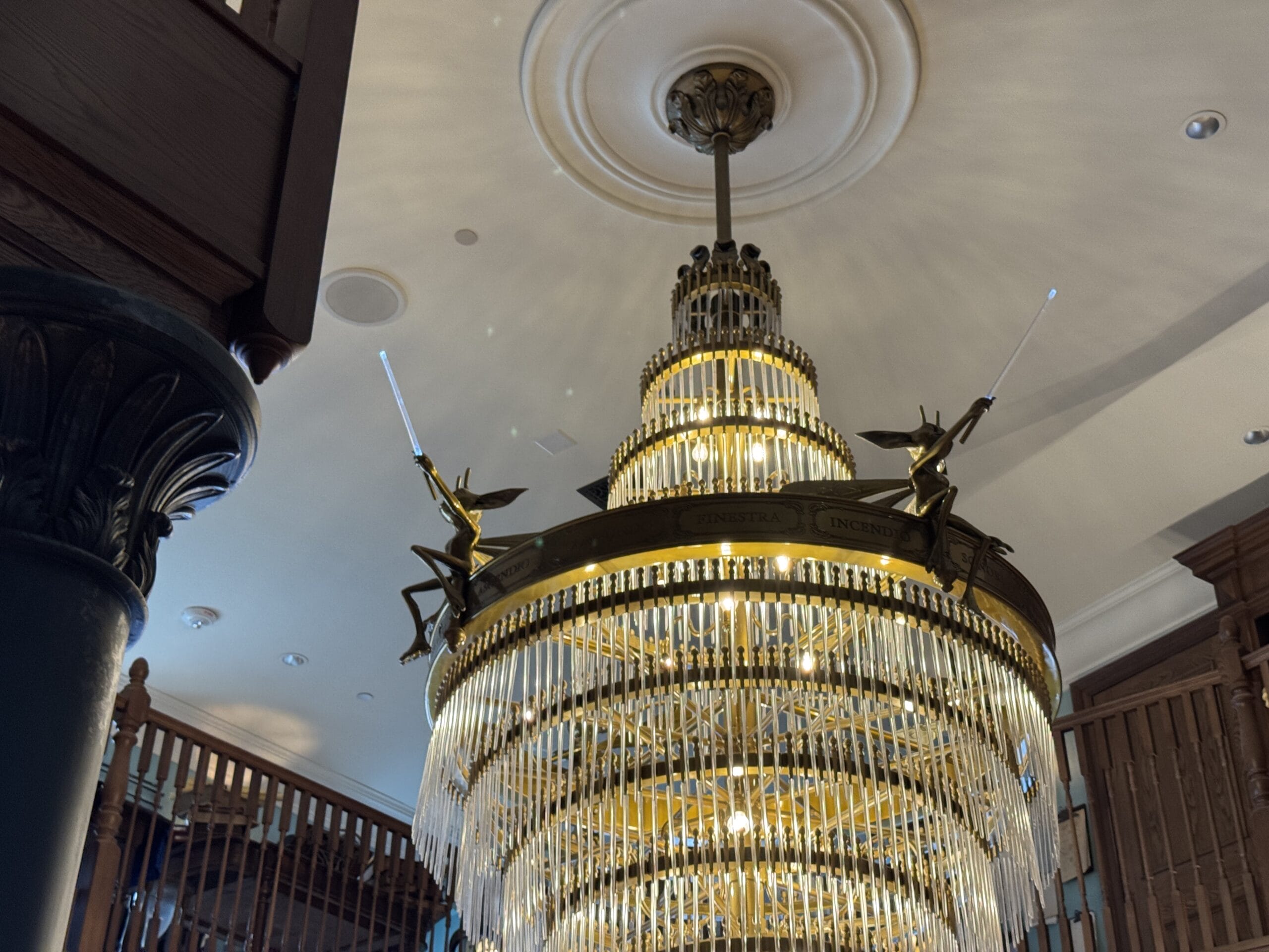 Large ornate chandelier with Cosme Acajor fairy sculptures holding baguettes magique, adorned with glass prisms.