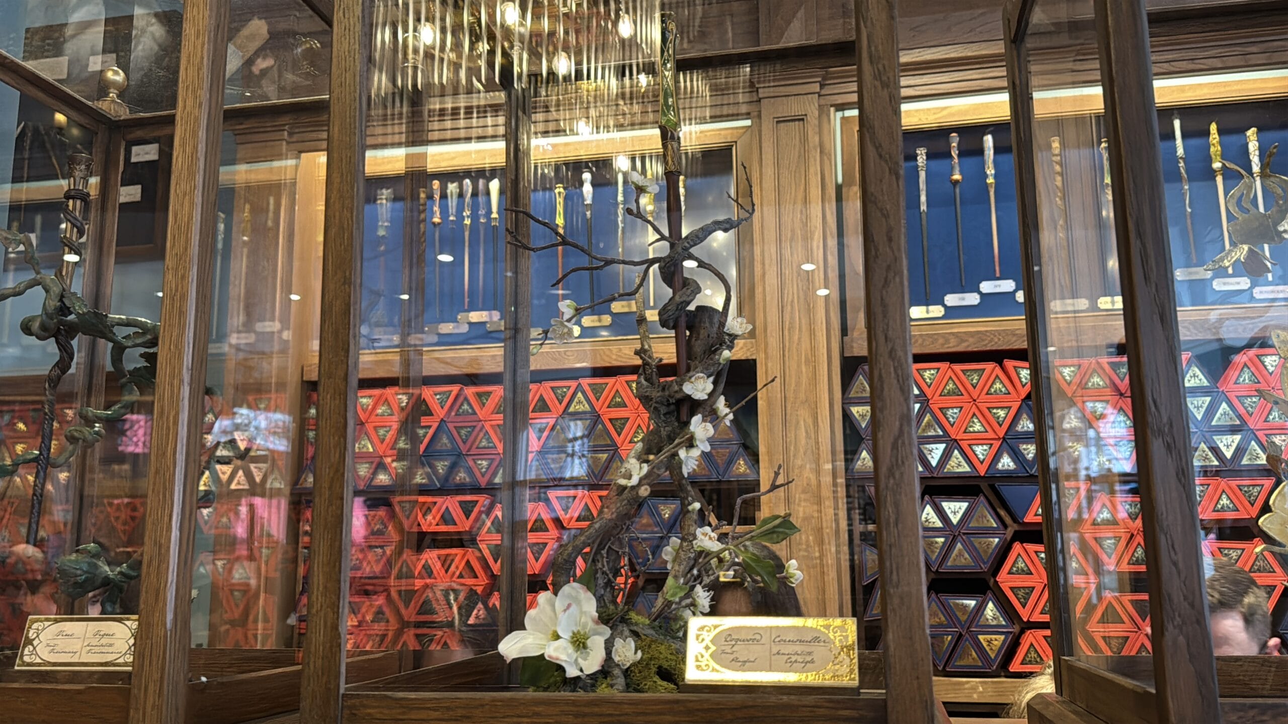Wooden display case with decorative tree, Cosme Acajor Baguettes Magique, and colorful triangle-patterned boxes.