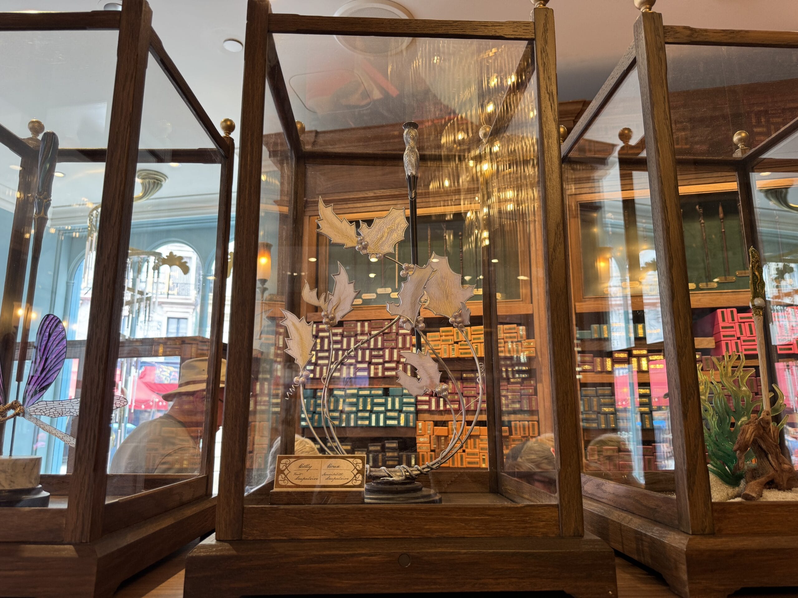 Glass display case with a Cosme Acajor Baguettes Magique sculpture of white leaves on a wooden base in a colorful shop.