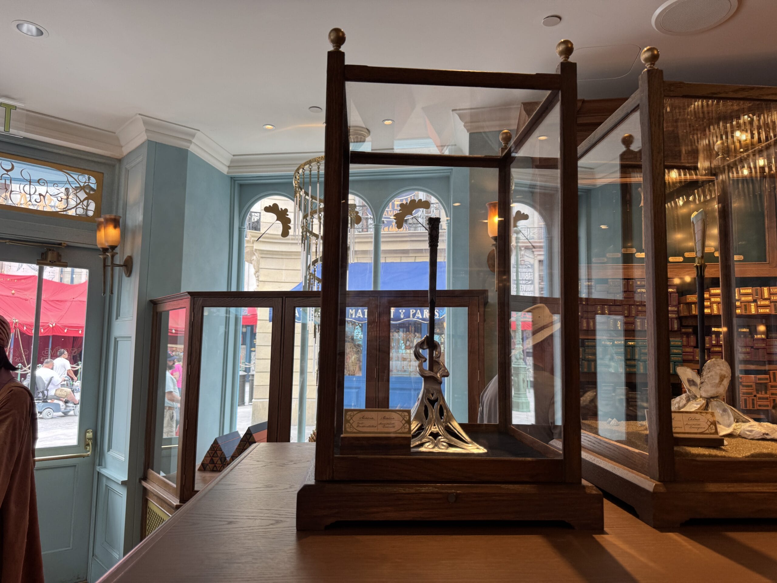 A glass display case holds a silver sword with a decorative hilt at Cosme Acajor Baguettes Magique shop.