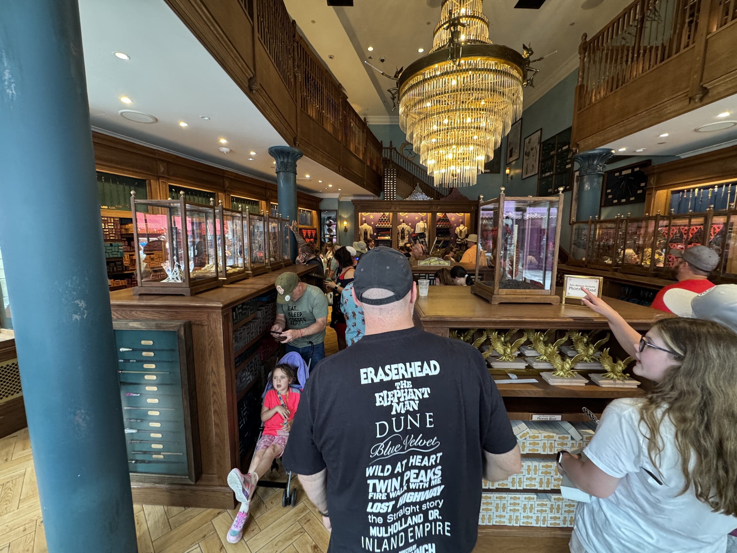 A crowded gift shop with Cosme Acajor Baguettes Magique, a chandelier, and people browsing merchandise.