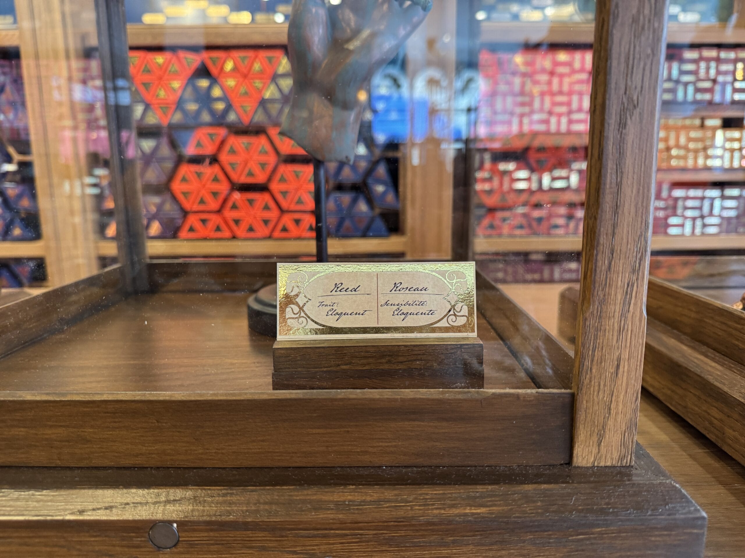 A display card labeled "Head" and "Bronze" in a wooden case, with Cosme Acajor Baguettes Magique blurred behind.