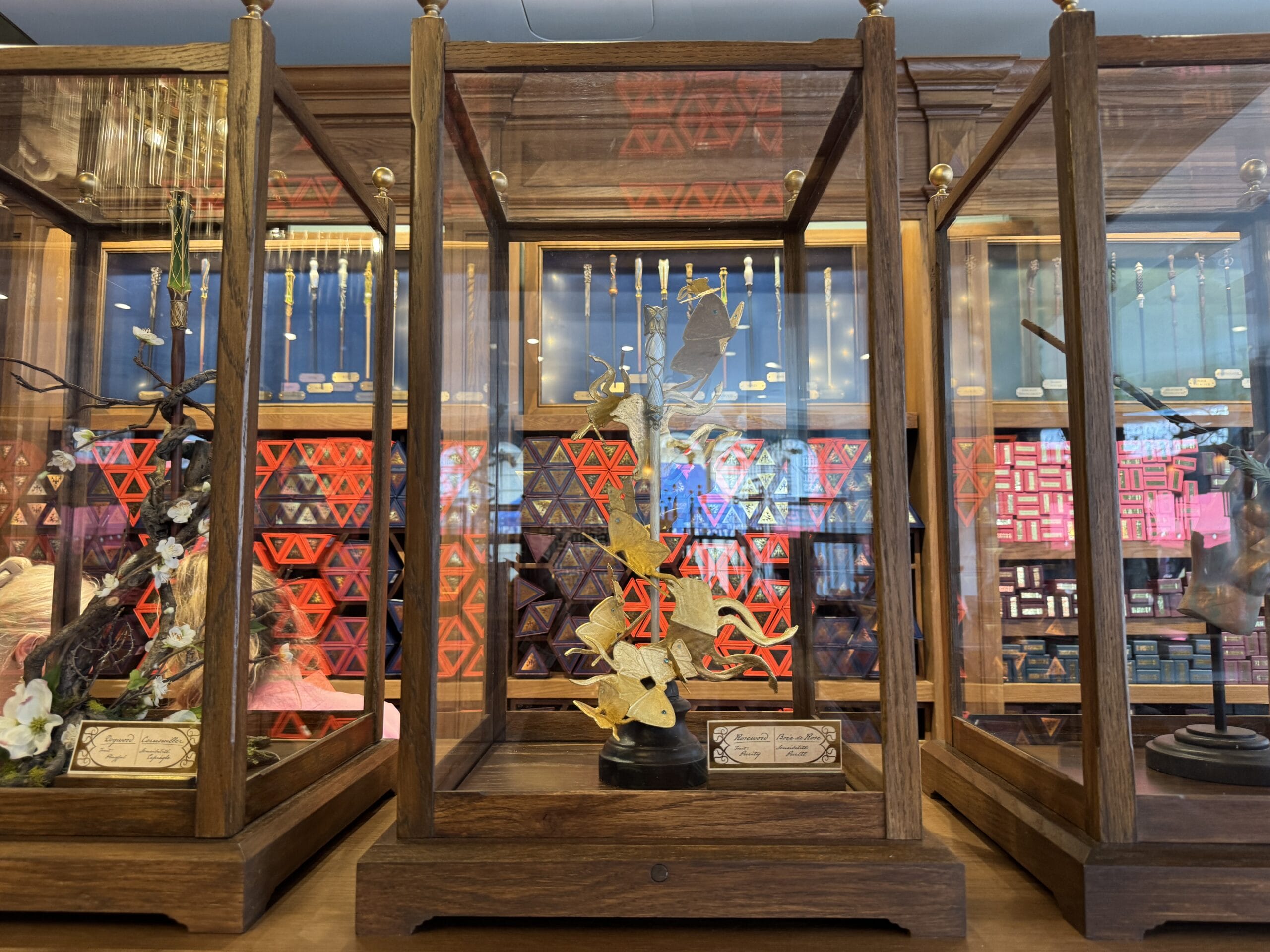 A delicate sugar phoenix sculpture by Cosme Acajor is displayed in a wooden and glass case, red patterns behind.