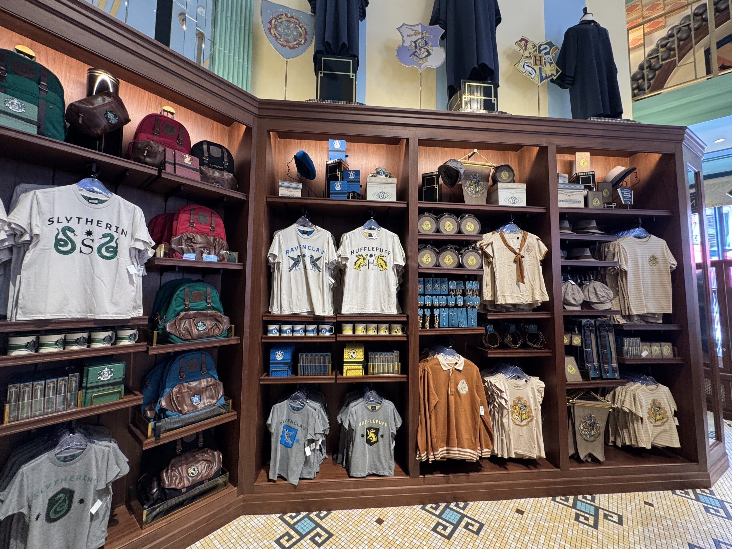 Shelves at Les Galeries Mirifiques display Harry Potter house-themed shirts, bags, and souvenirs by each Hogwarts house.