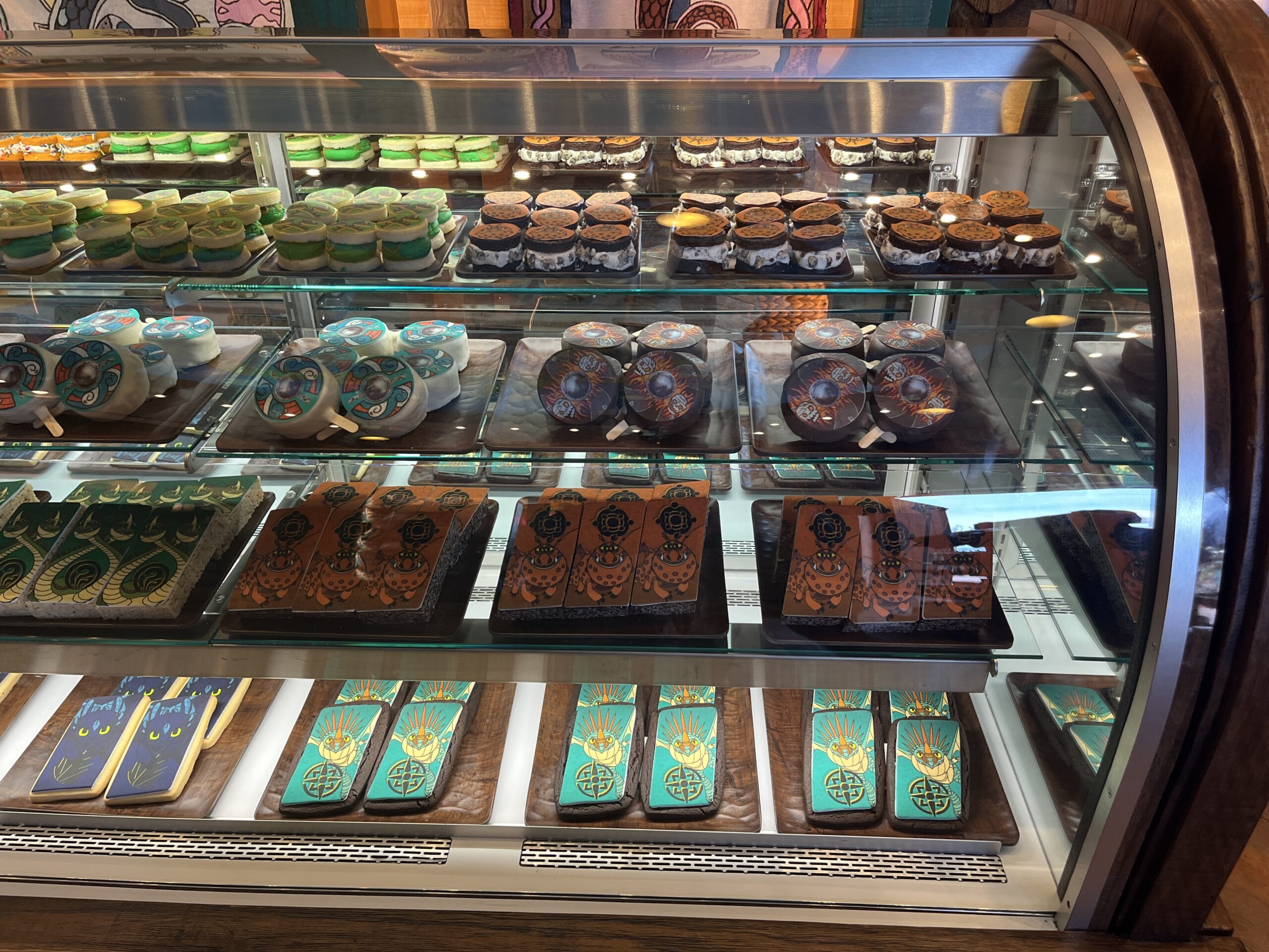 A bakery display case filled with colorful, How to Treat Your Dragon-themed cookies and desserts in fun shapes.