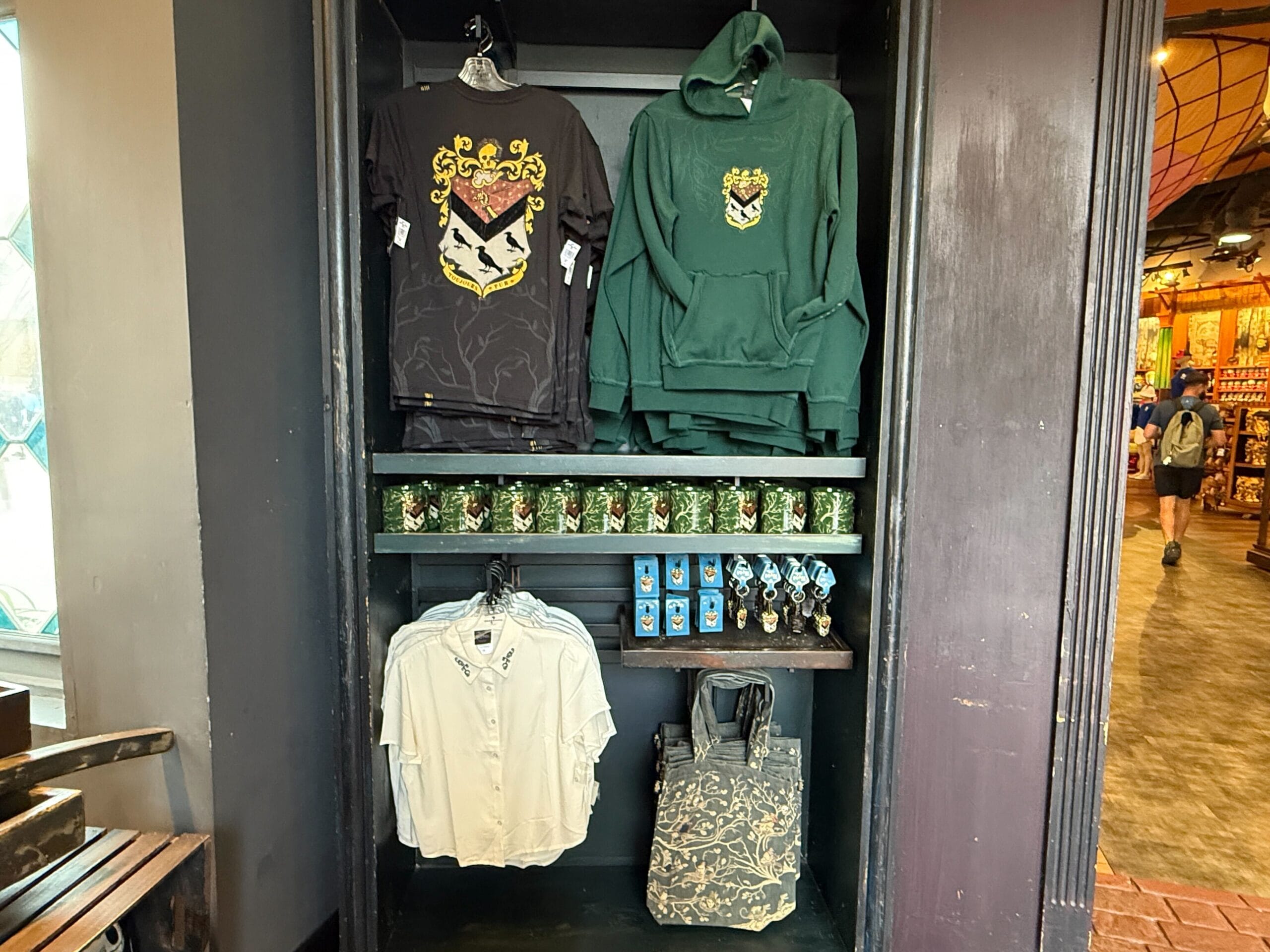 Display of Slytherin merchandise at Universal Studios Orlando, featuring shirts, mugs, pins, and House of Black items.